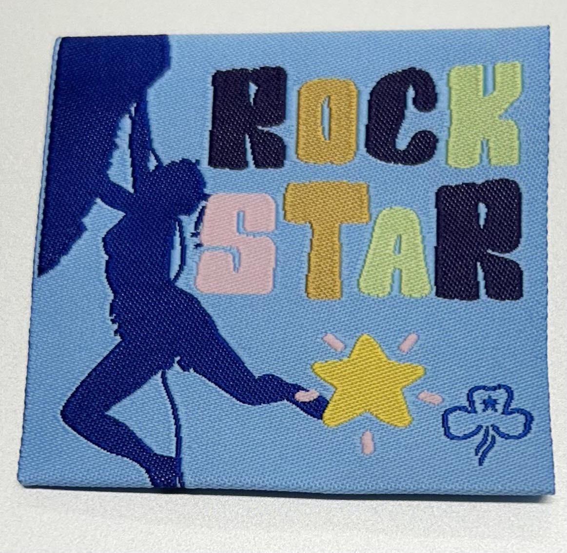 a square unbound badge with a girl abseiling and a yellow star with the words rock star