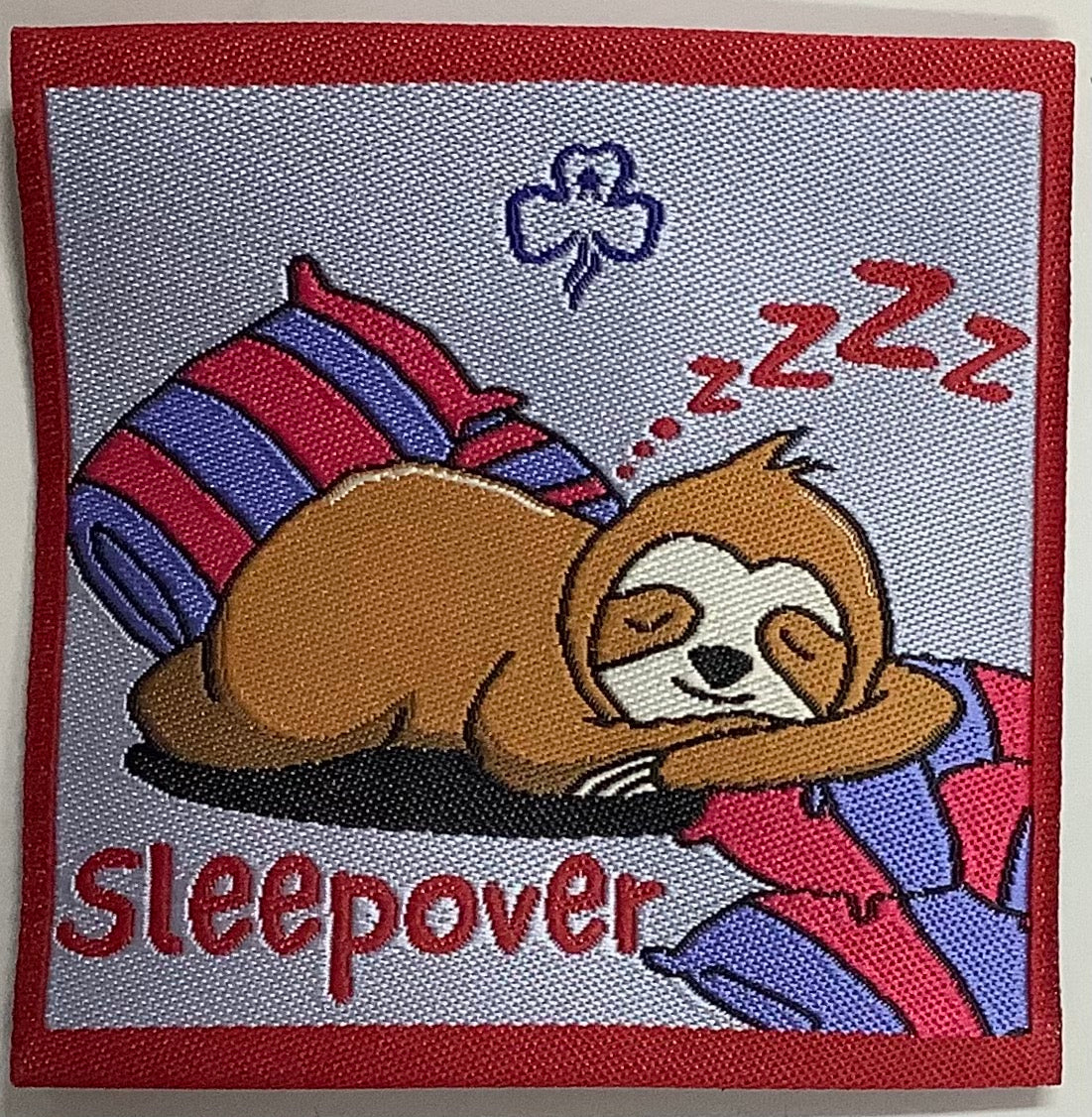 a square unbound badge with a sloth and a sleeping bag