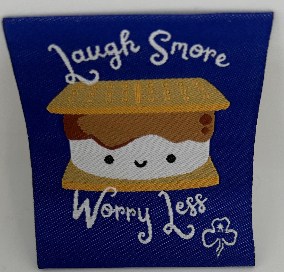 a square unbound fun badge that is royal blue in colour with a picture of a smore with the words laugh smore worry less