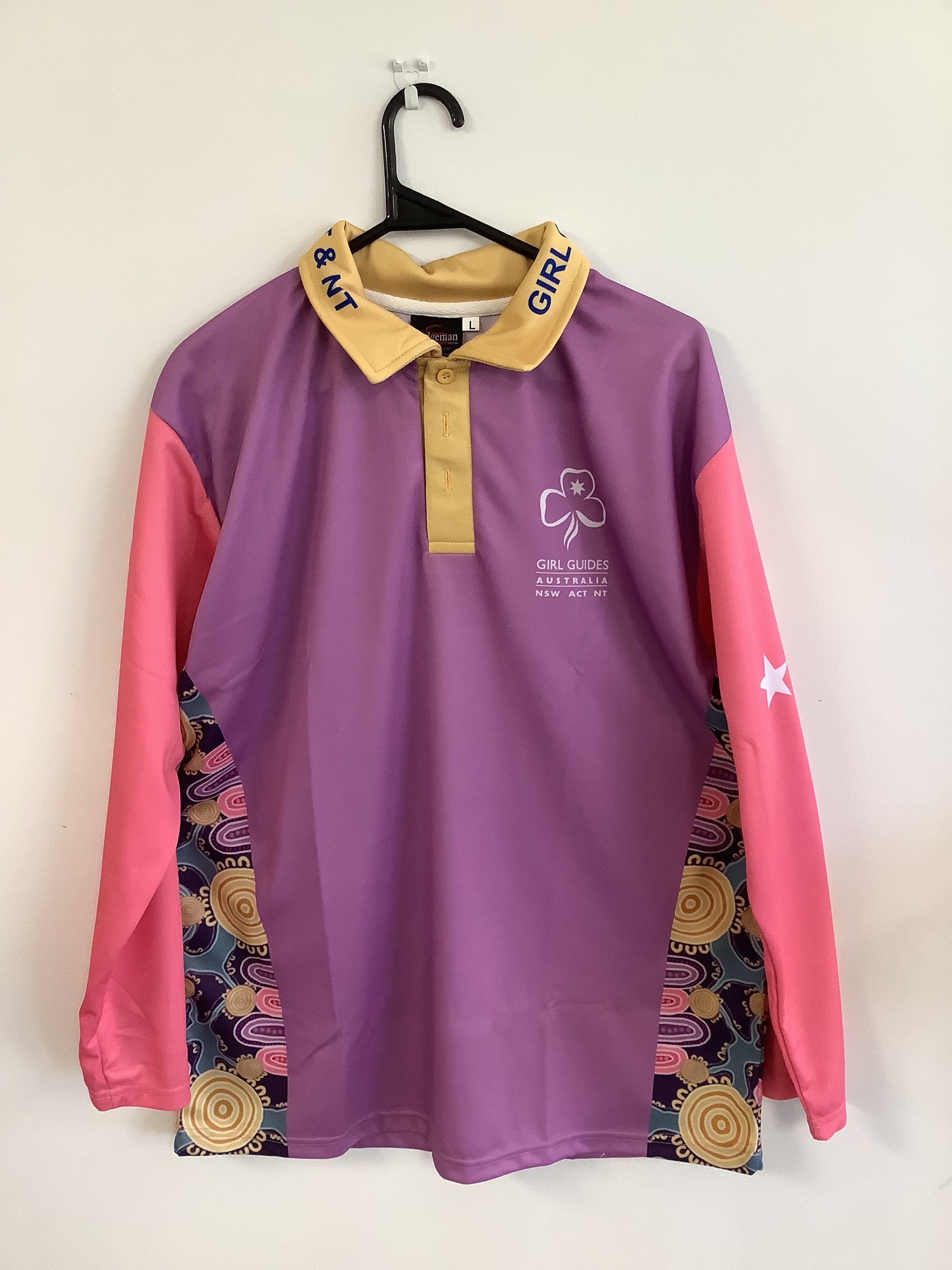 a long sleeved polo shirt with pink sleeves, purple body with aboriginal art on the sides and a gold collar