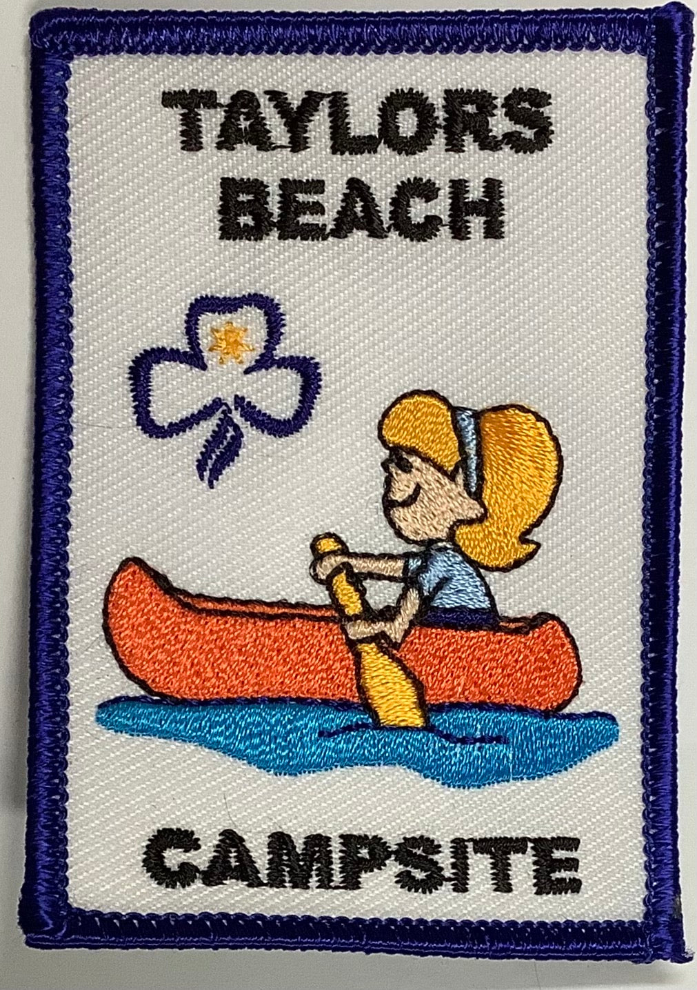 a rectangular badge bound in blue with a girl in a canoe
