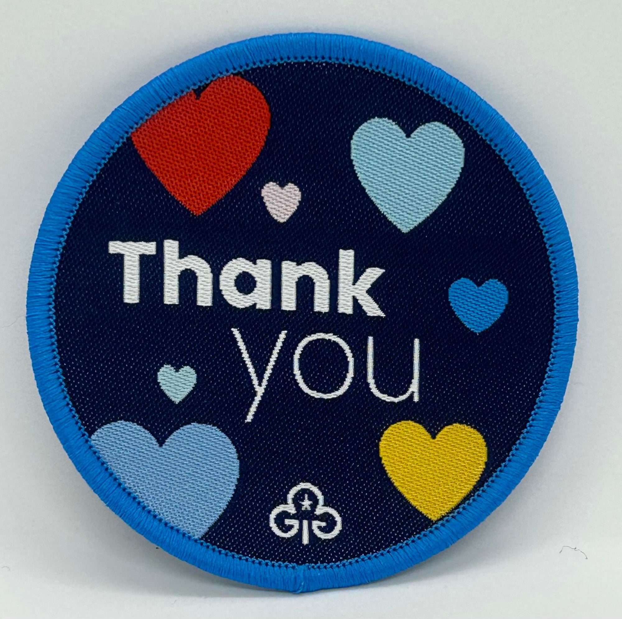 a round blue badge bound in light blue with thank you  and hearts