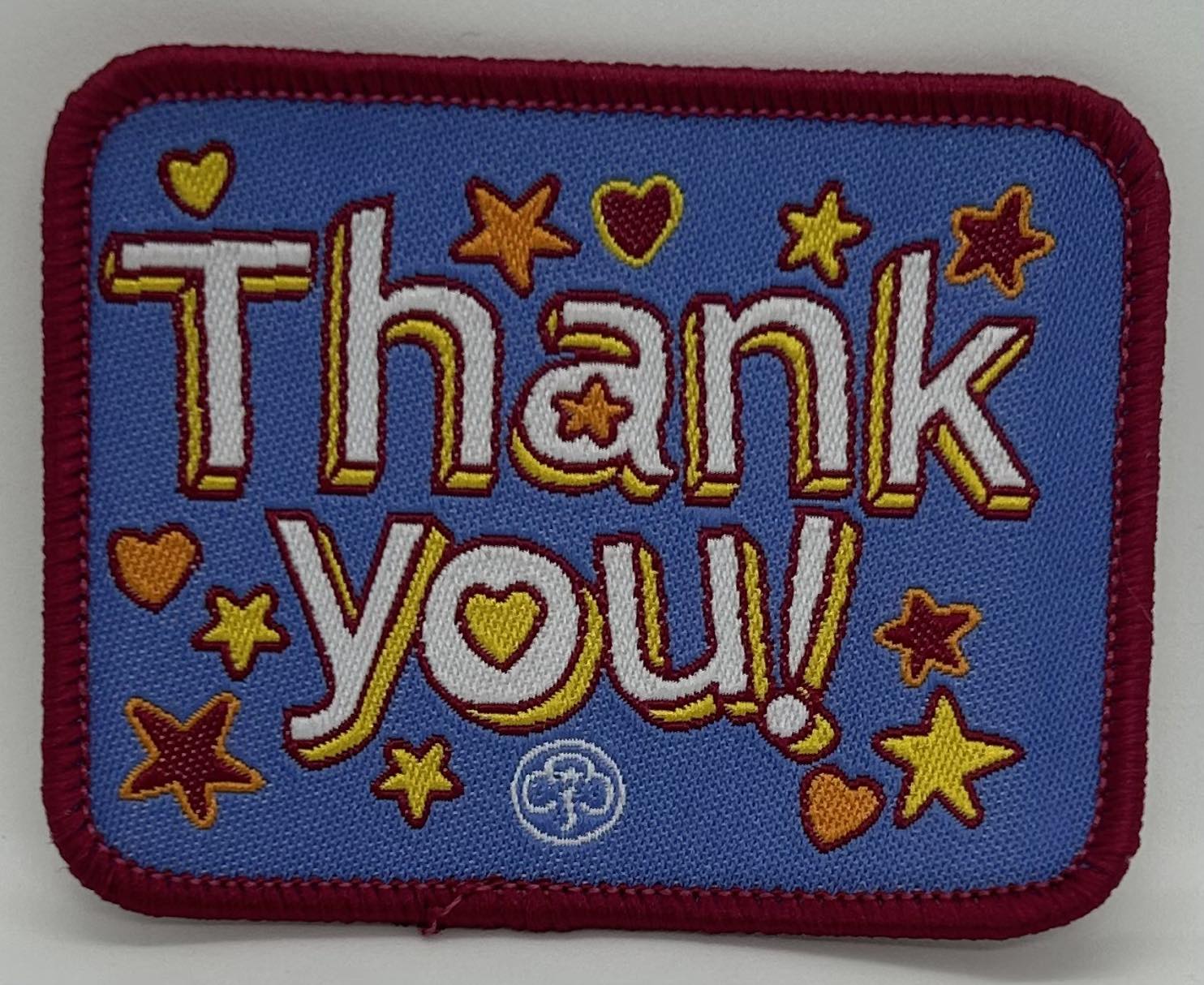 a square badge bound in red with thank you in white with hearts and stars