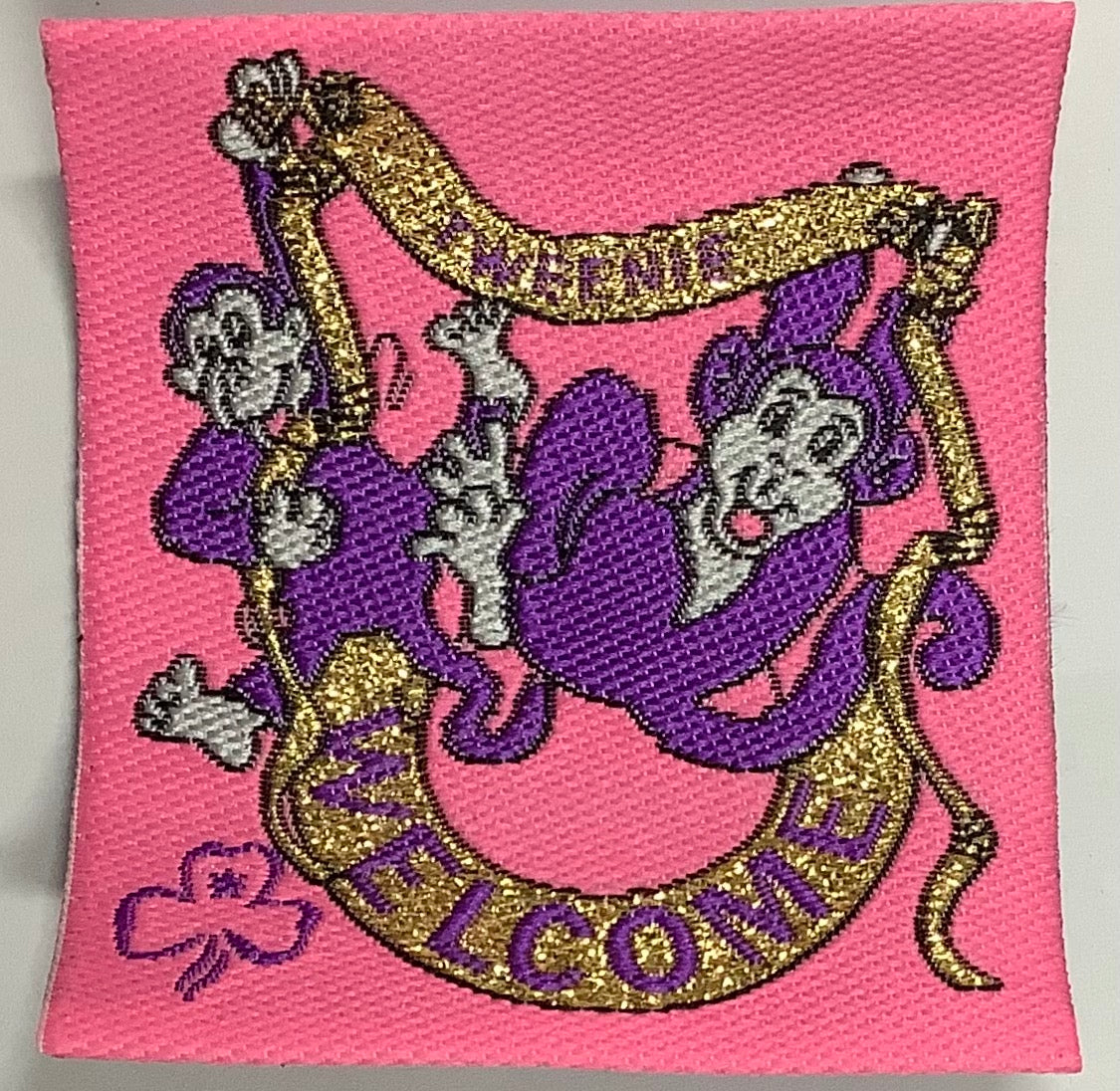 a square unbound bright pink badge with purple monkeys and gold ribbon