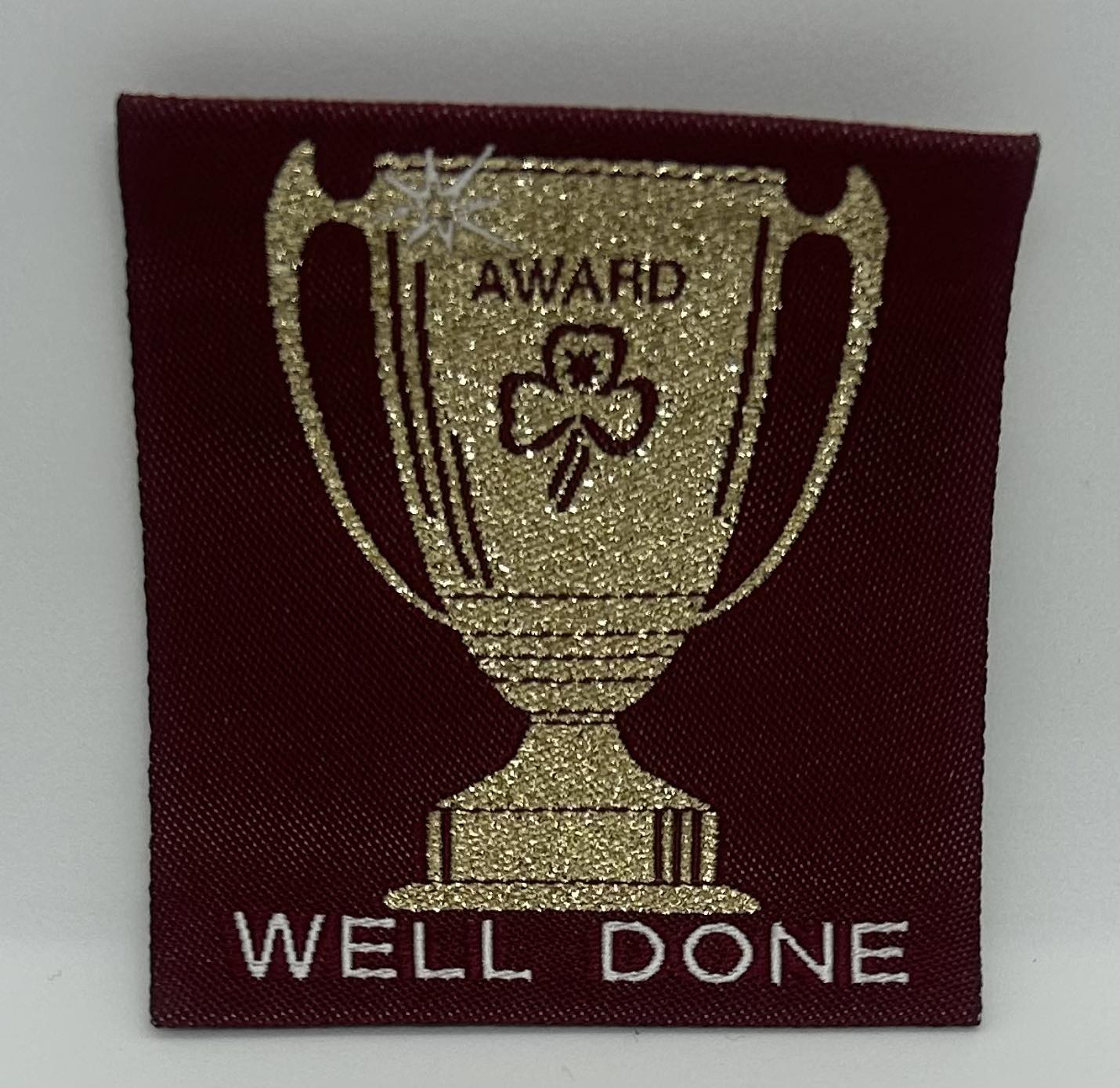 a square maroon unbound badge with a gold trophy