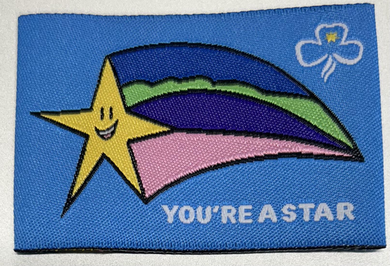 an unbound rectangular badge that is light blue background with a yellow star with coloured stream behind the star