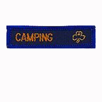 blue rectangle woven badge with the word camping sewn in gold in capital letters and a gold trefoil after the writing