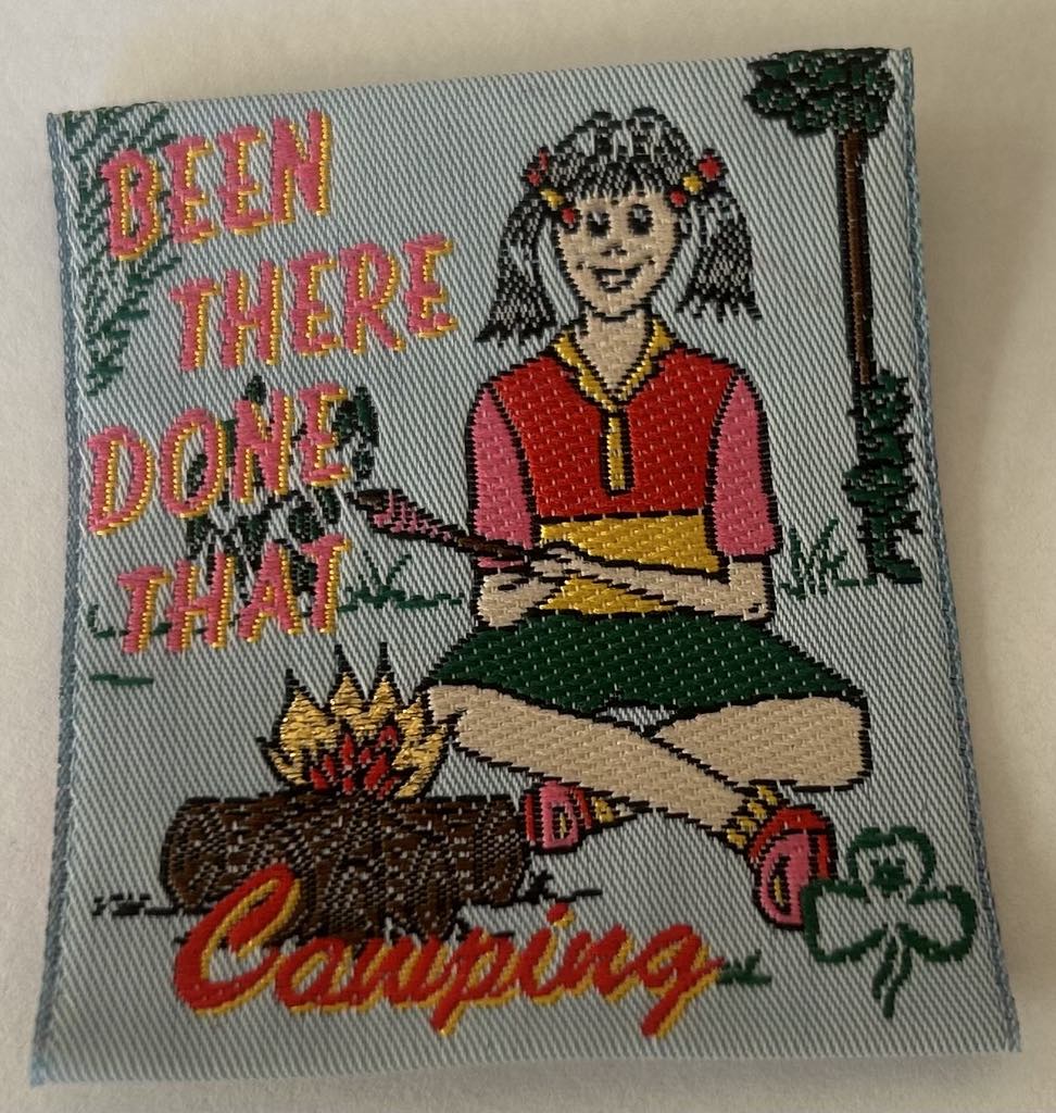 a square unbound badge with a girl at a campfire