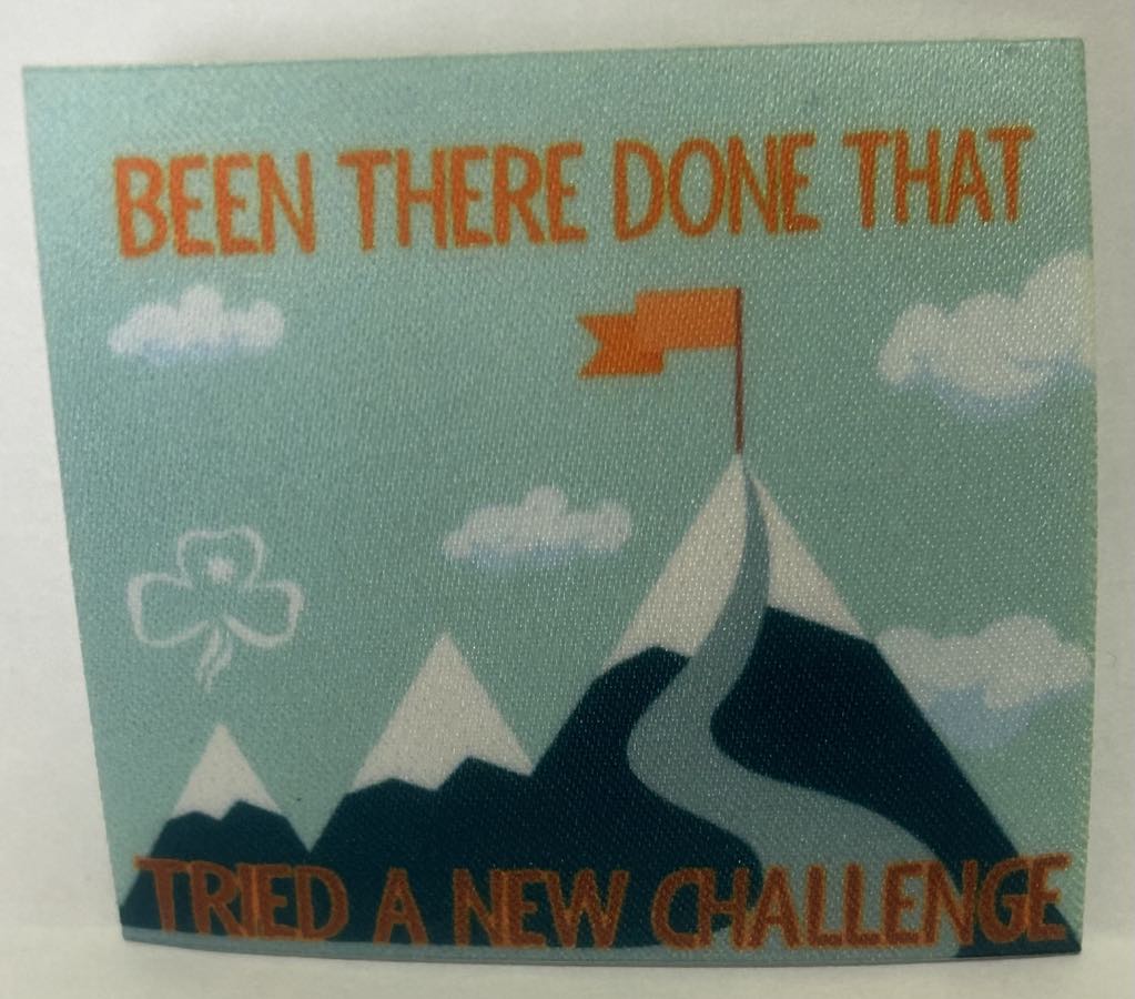 an unbound badge with a flag on a mountain top with the words been there done that tried a new challenge in orange
