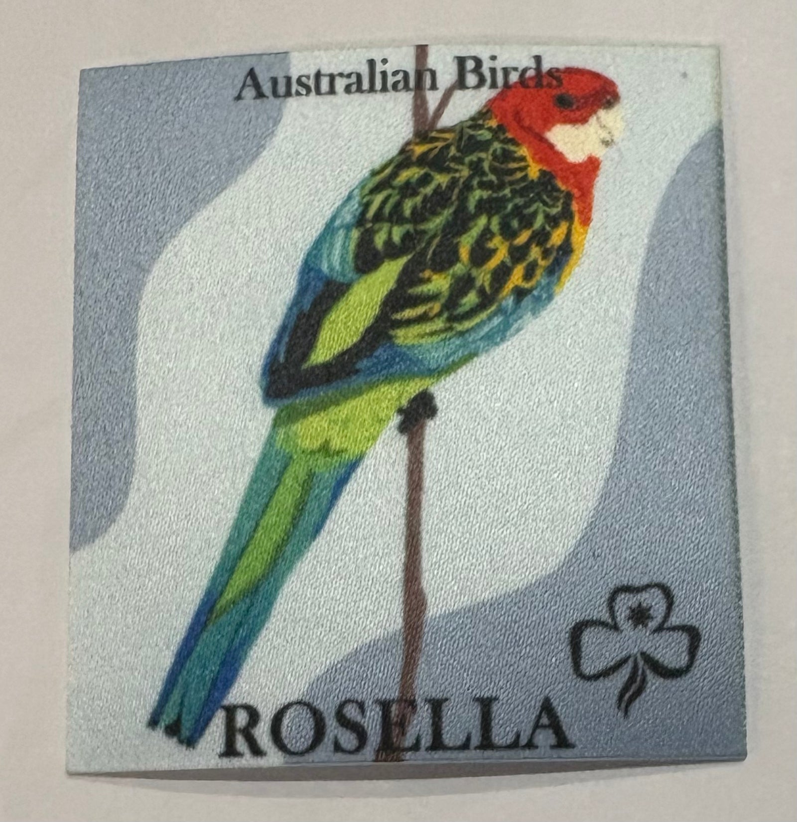 A square unbound grey badge with a rosella