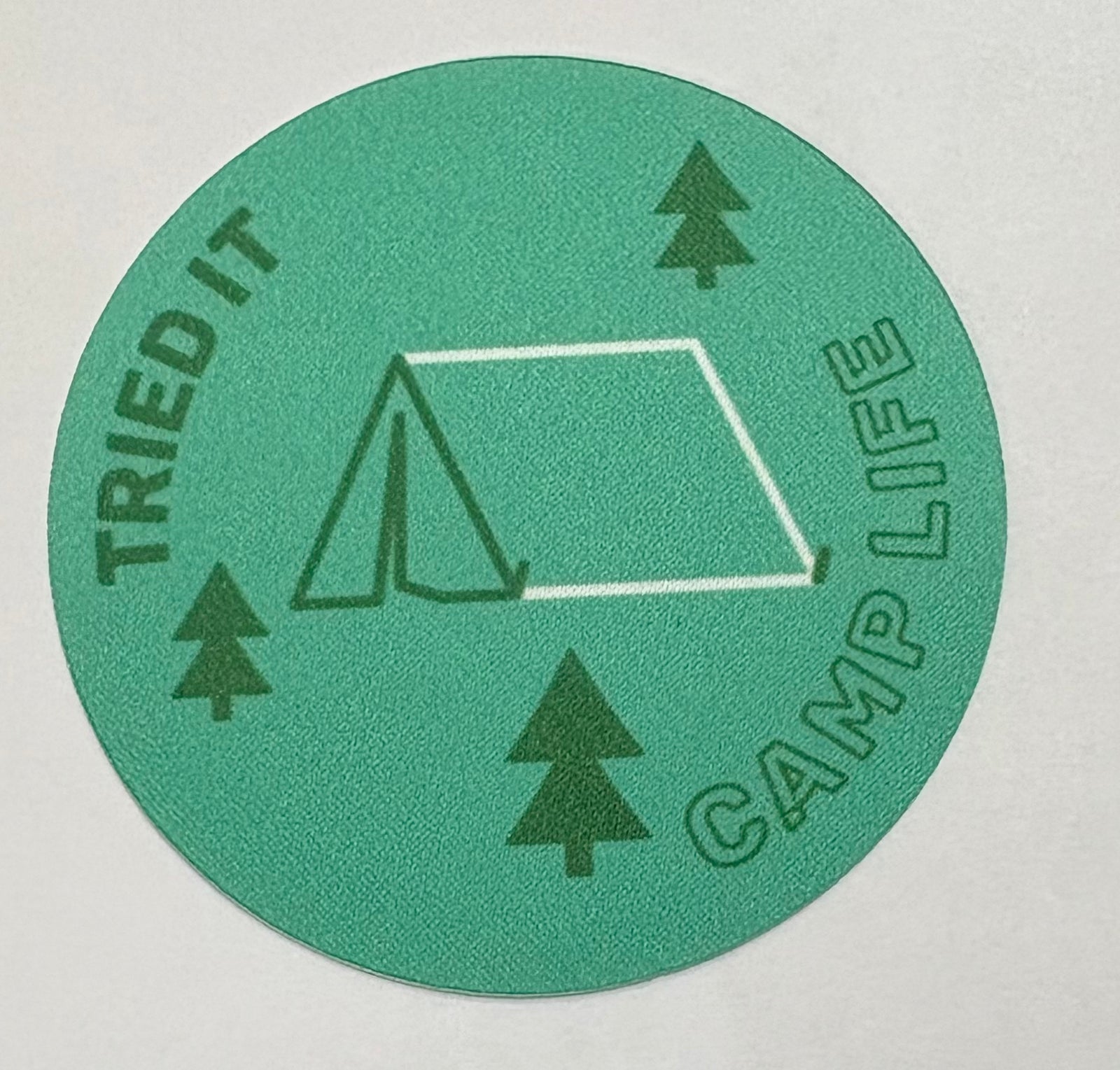 Round unbound green badge with a tent and some trees 