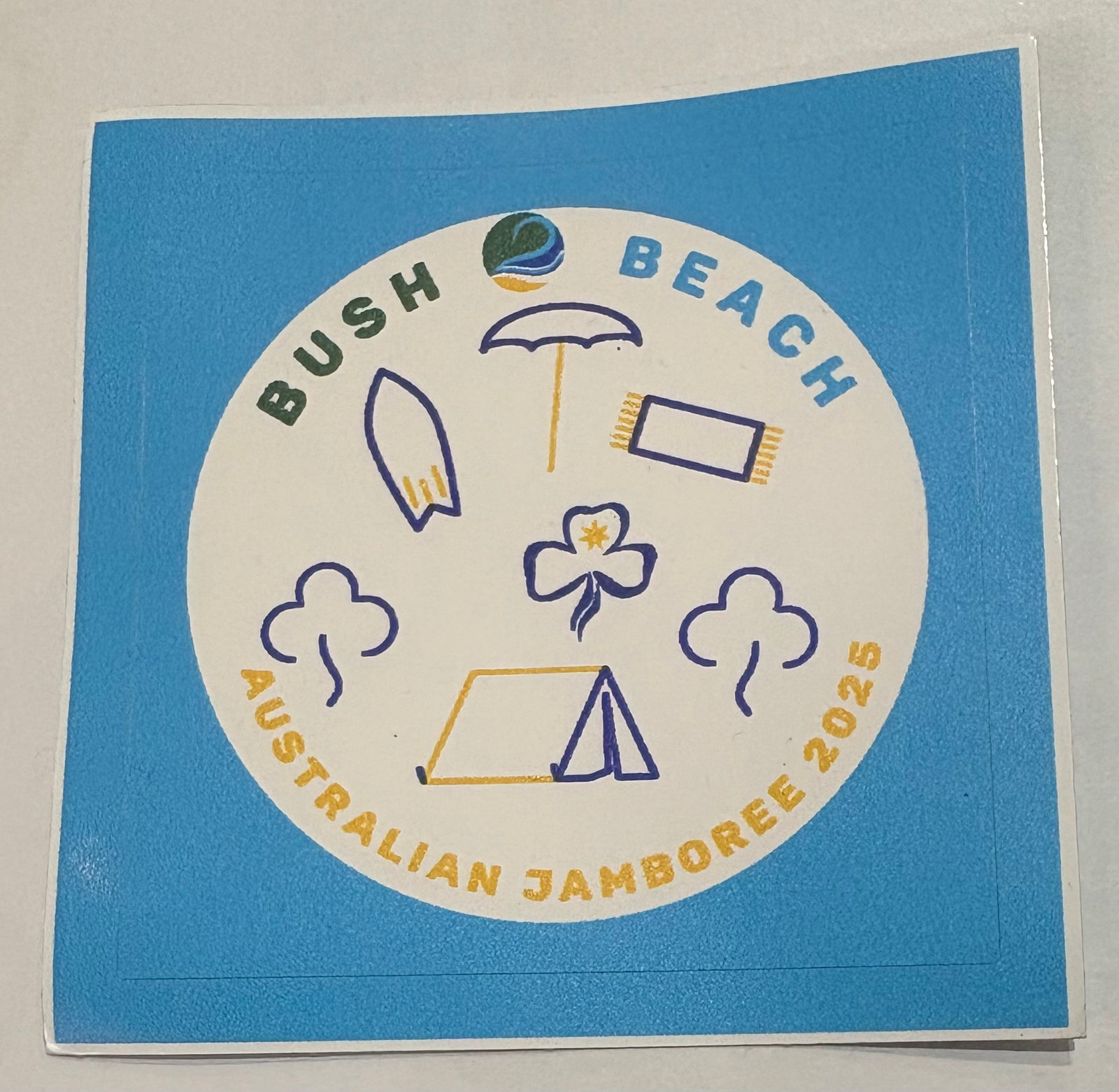 A round sticker with bush 2 beach jamboree and a tent, trees, beach towel, trefoil and umbrella 