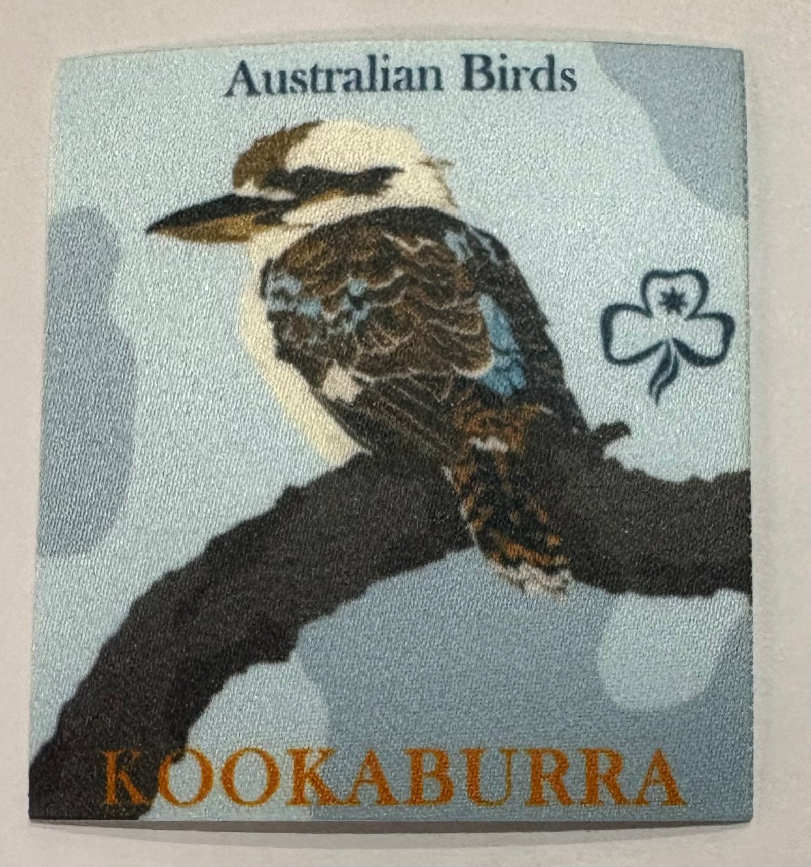 A square unbound badge with a kookaburra sitting on a branch 