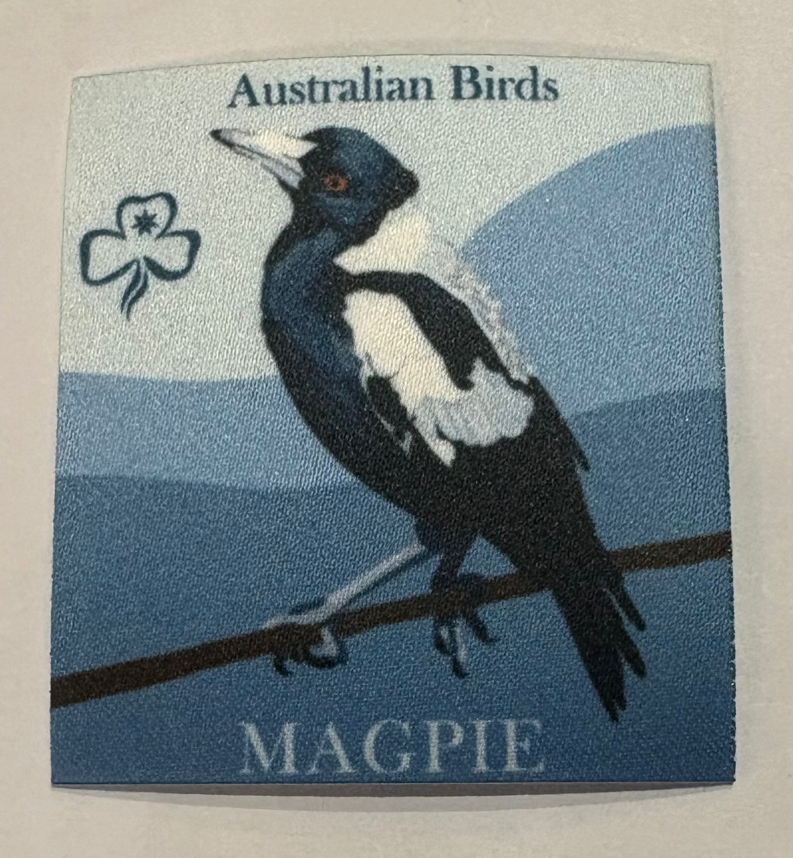 A square unbound grey badge with a magpie 