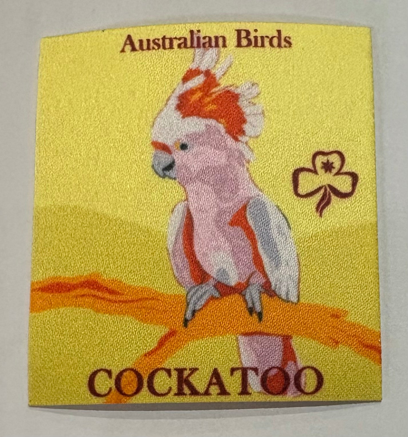 A square unbound yellow badge with a cockatoo on a golden branch
