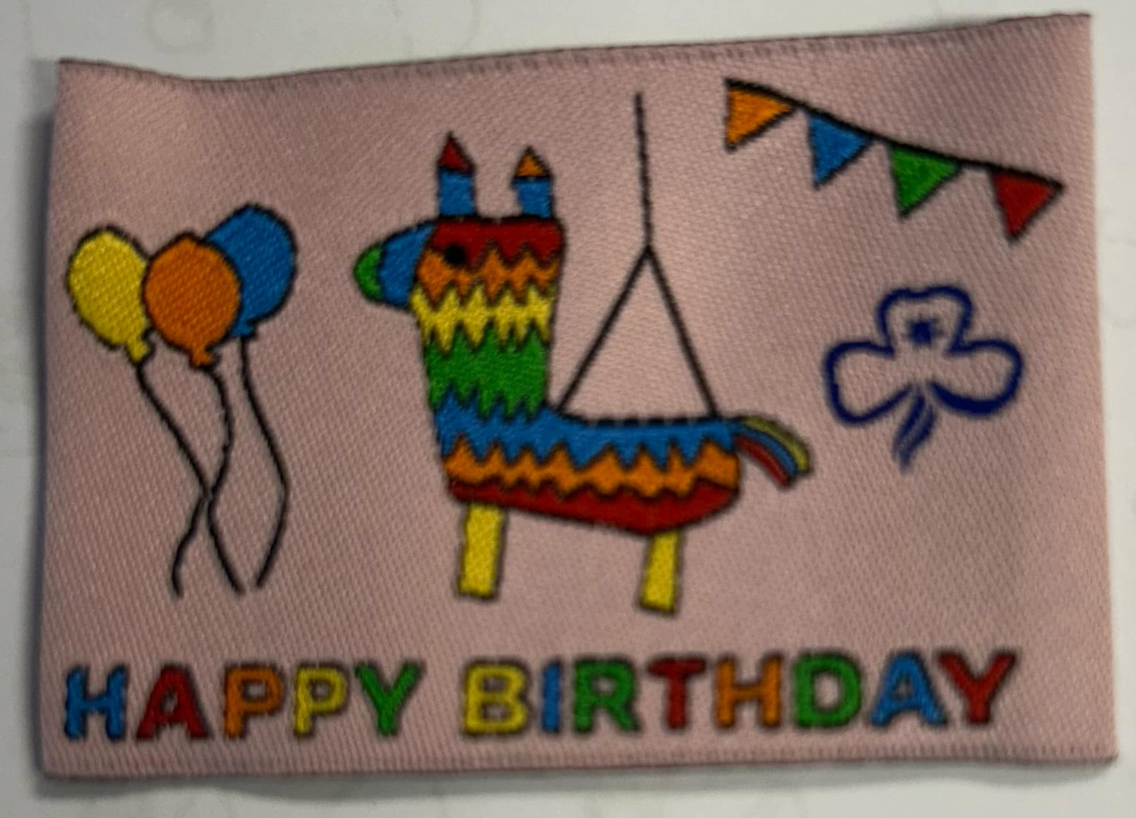 a rectangular light pink badge with a piñata horse shaped and balloons and streamers