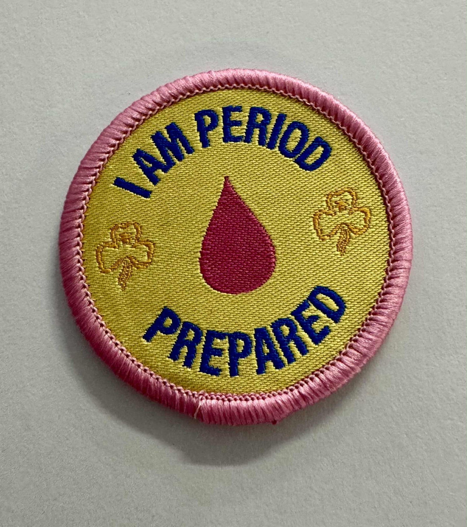 A round yellow badge bound in pink with the words I am period prepared with a pink droplet 