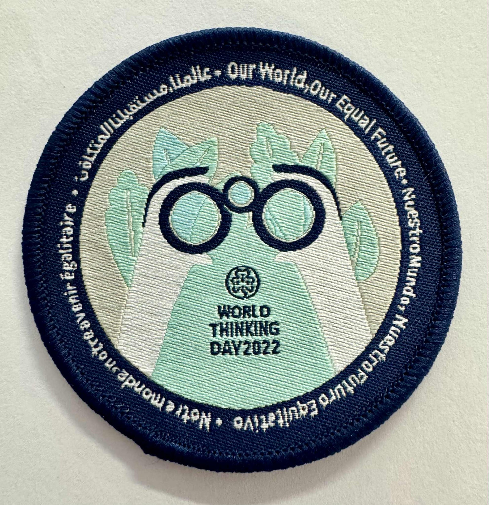 A round badge bound in blue with hands with circles in the shape of binoculars 