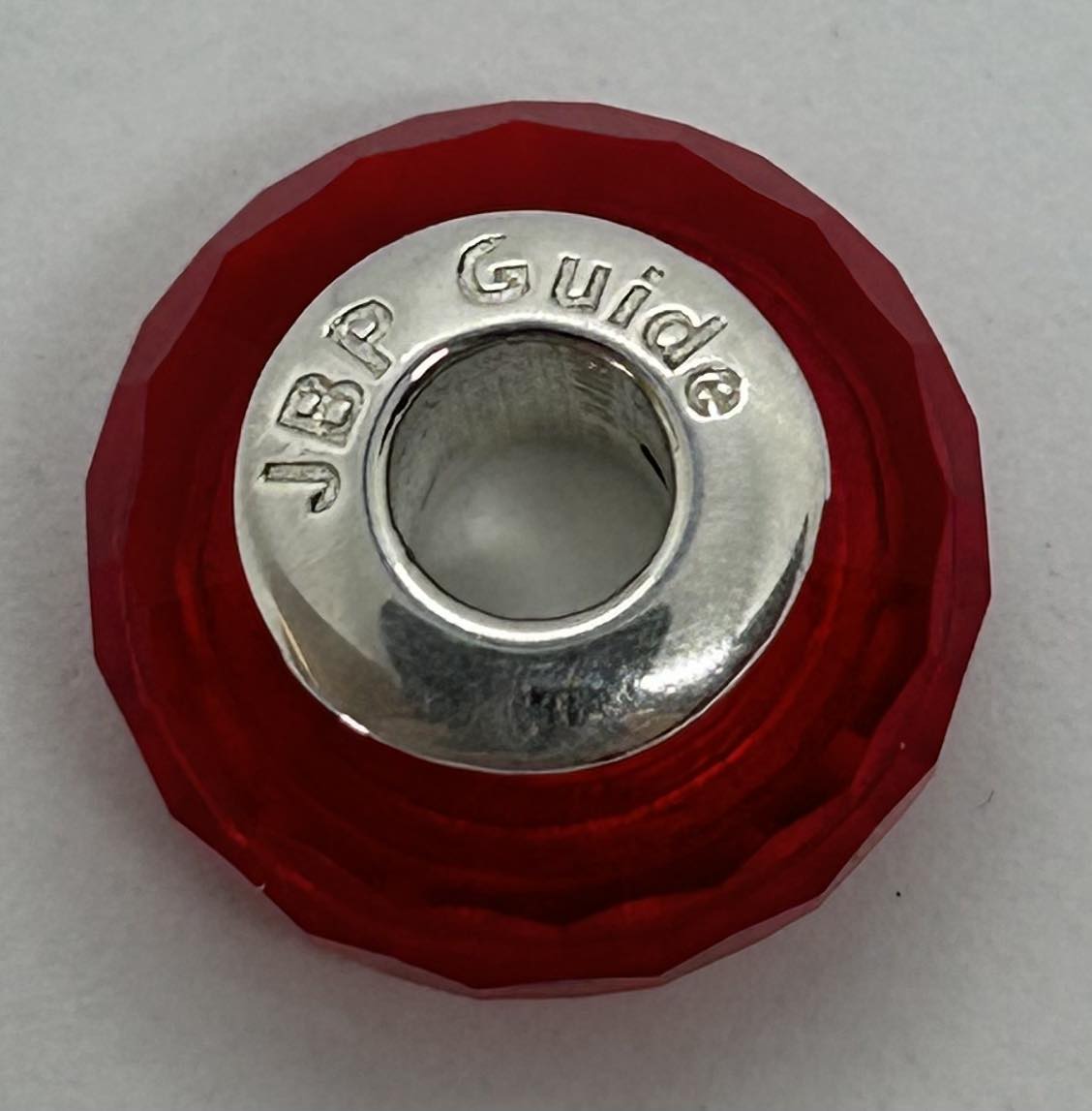 a pandora style bead that has a red bead with a silver centre with JBP Guide in the centre