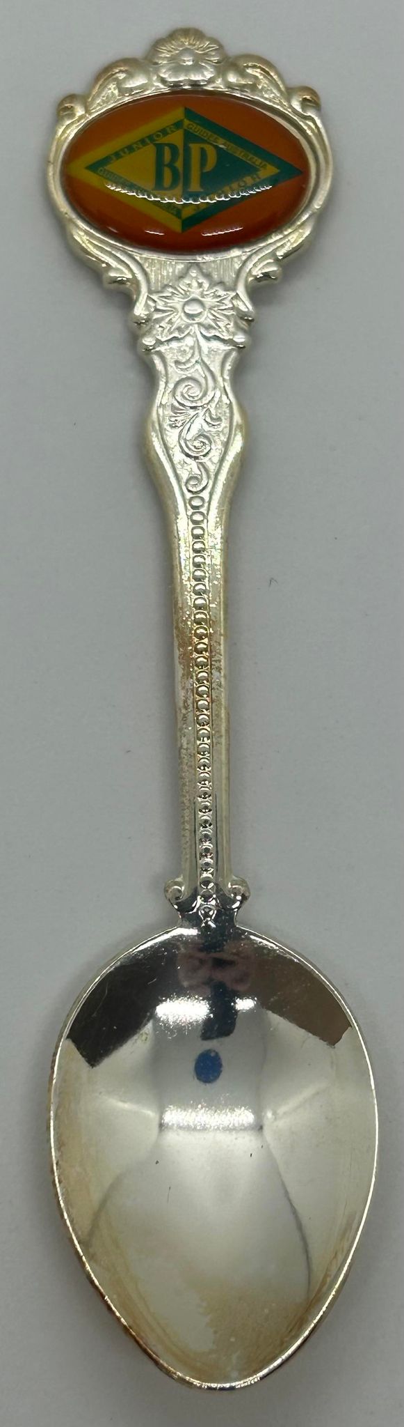 a metal spoon with an enamel top with the JBP award emblem