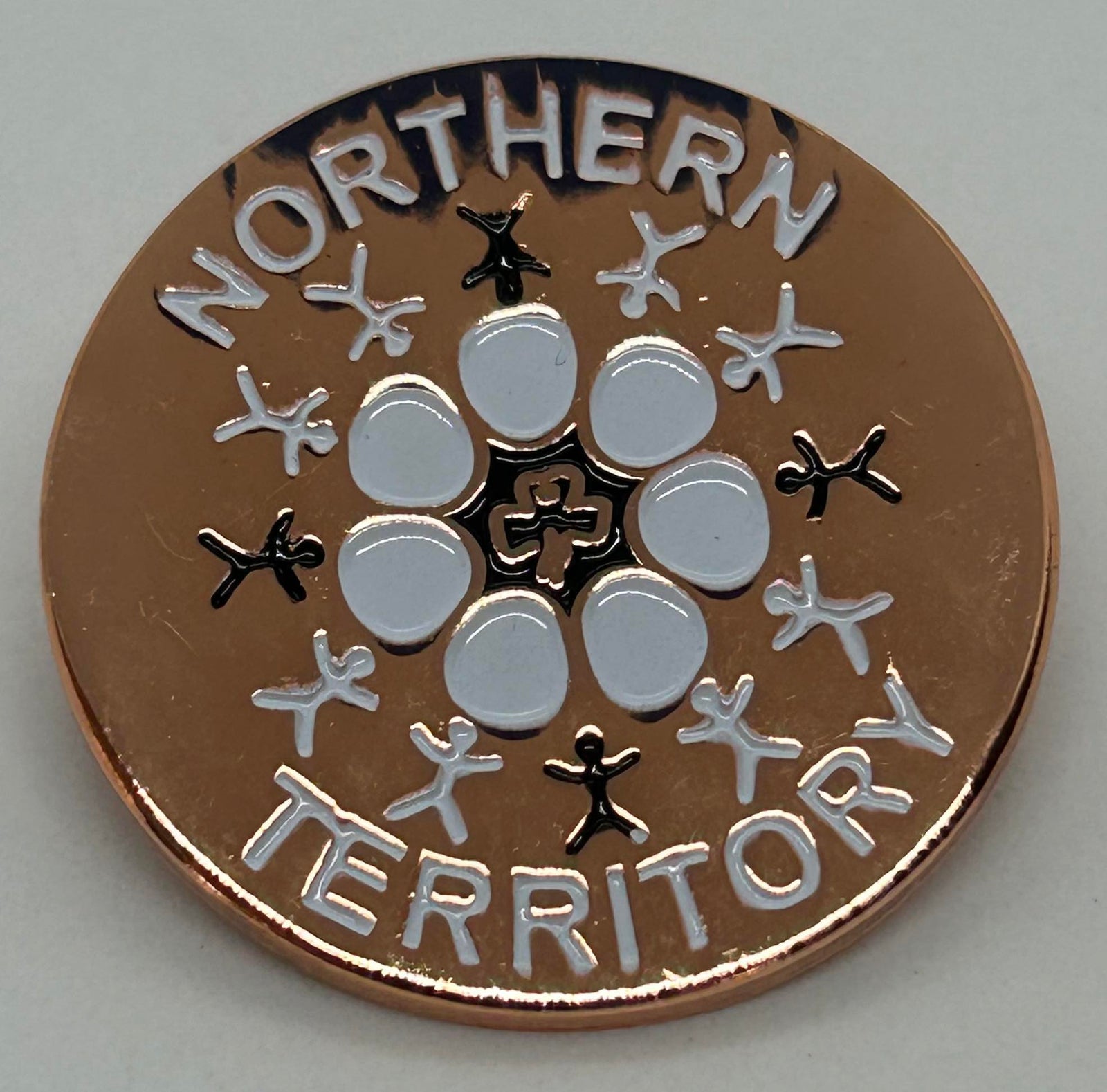 a round metal badge with a brown enamel front with people and a flower on it
