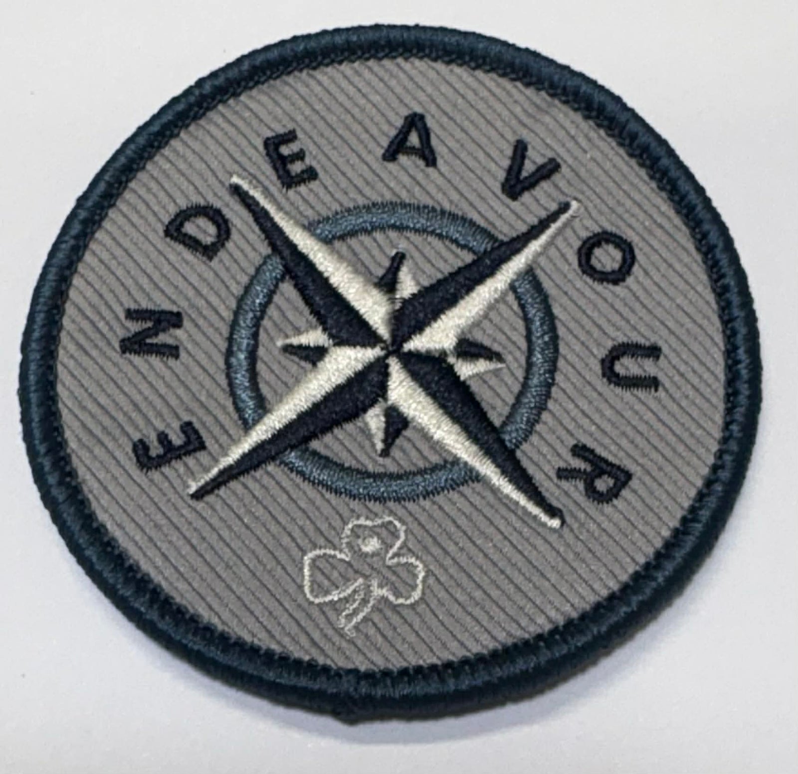 Circular silver badge with compass design and 'Endeavour' text on a grey background