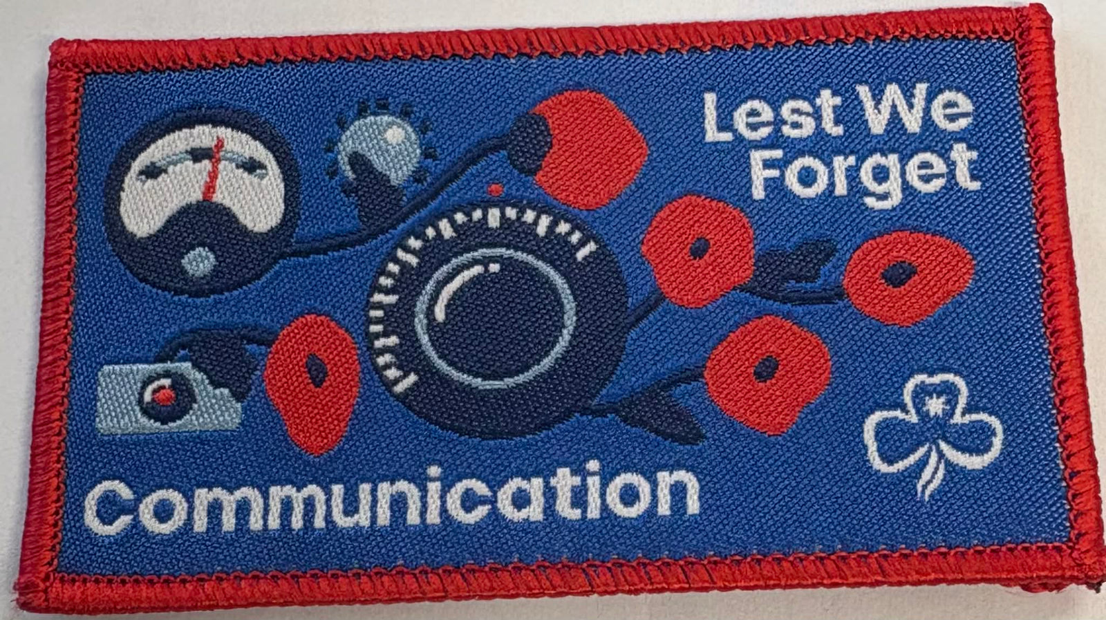 Bound badge with communication-themed design featuring a submarine, flowers, and text 'Lest We Forget'.
