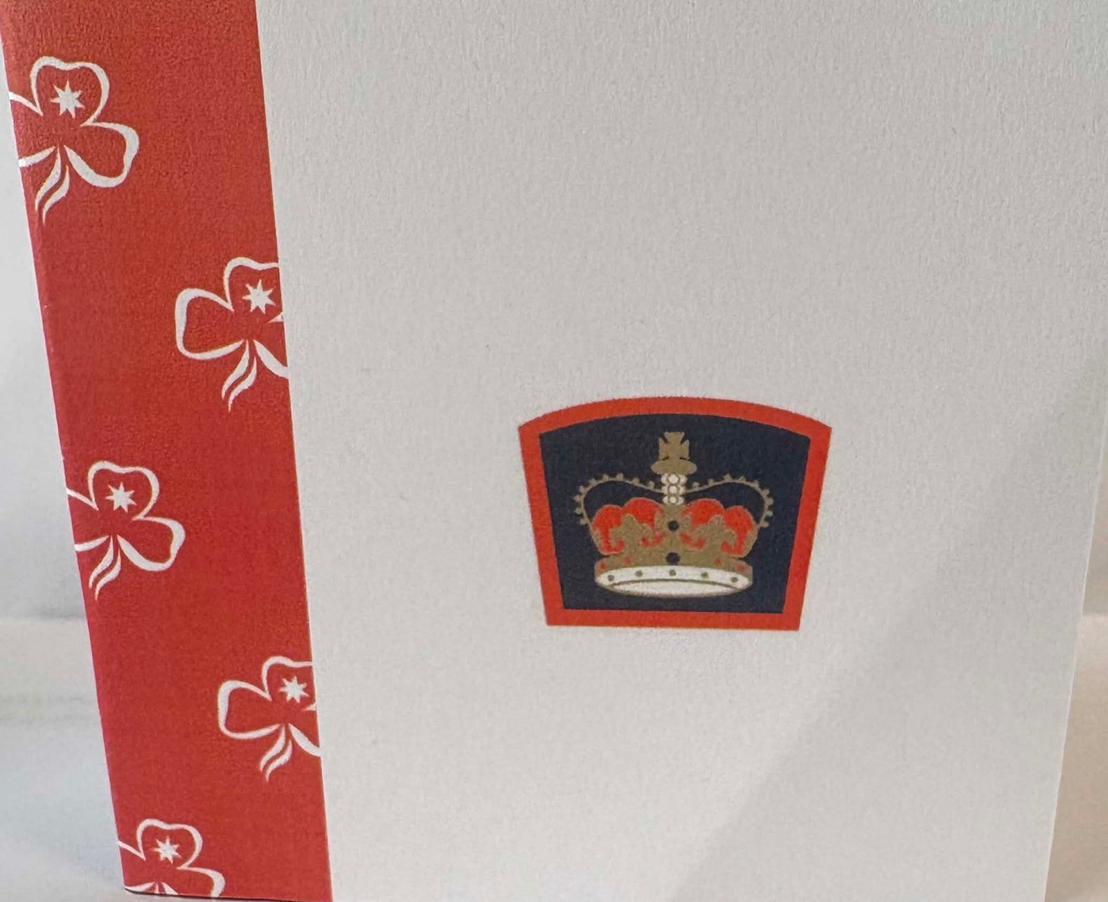 a small card with the queens guide badge emblem and red and white trim with trefoils