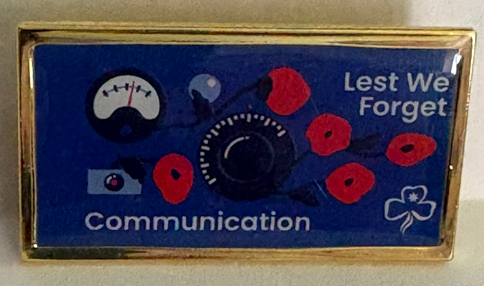 metal badge  with communication-themed design and 'Lest We Forget' text on a blue background
