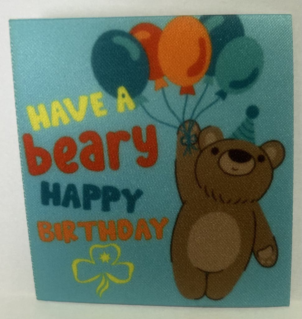 a square unbound badge with a teal background with a bear holding a bunch of balloons with the words have a beary happy birthday