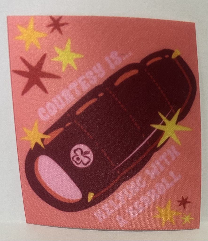 a square unbound badge with a pink background with a sleeping bag with the words courtesy is helping with a bedroll