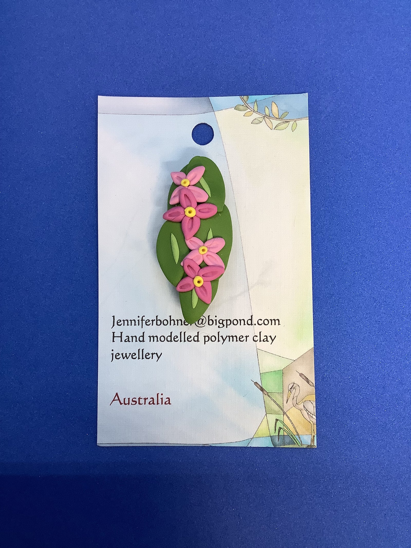 a clay brooch with a green leaf with pink flowers on it