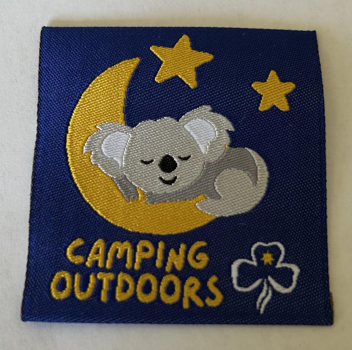 a square unbound blue badge with a koala sleeping on a quarter moon with two stars