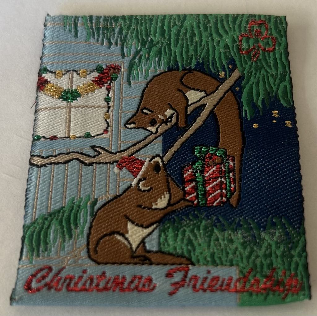 a square unbound badge with a possum on the ground passing a present to a possum in a tree outside a house at night time