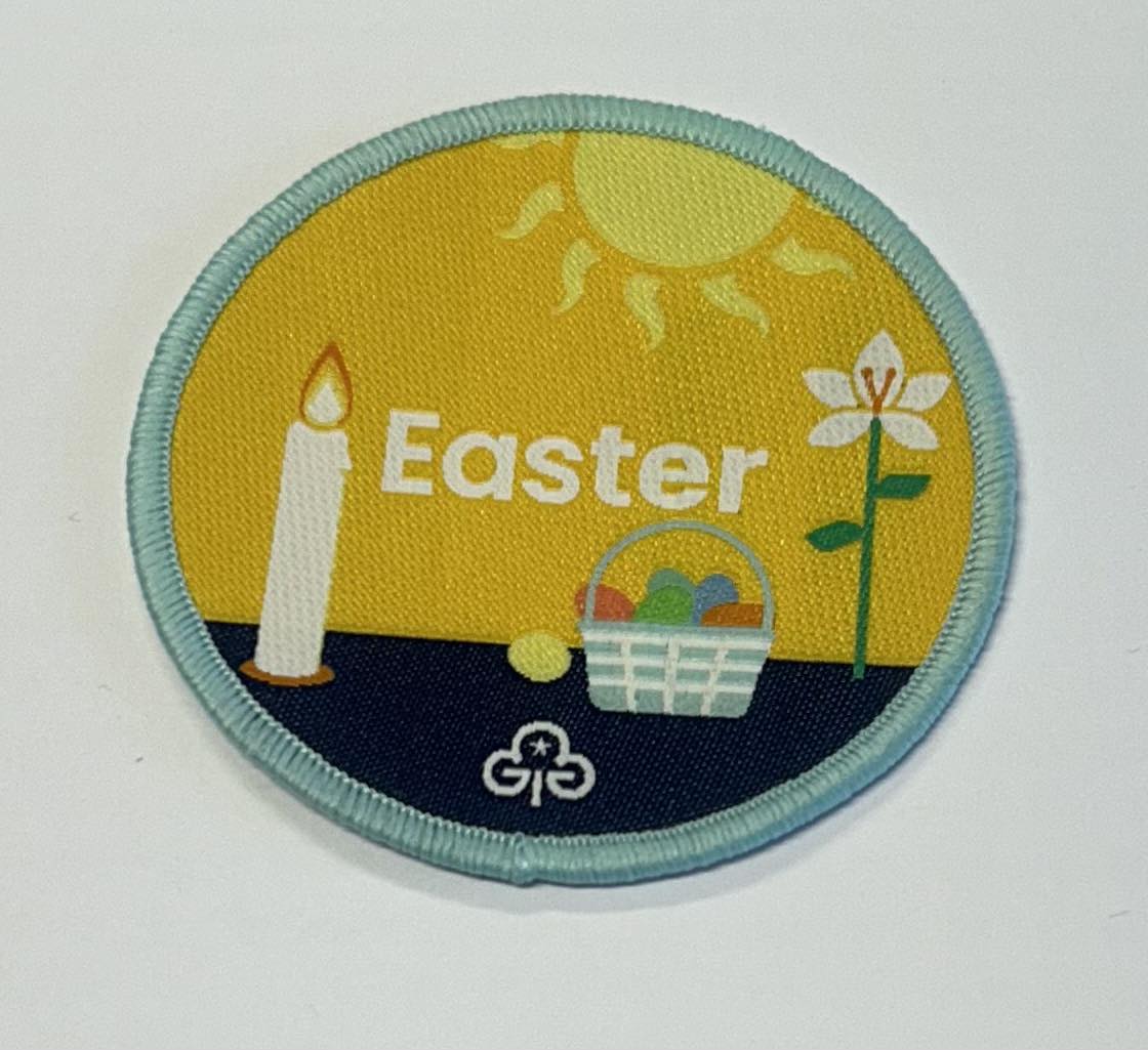 a round badge bound in green with a gold and blue background with the word Easter with a flower, candle and easter basket on the front