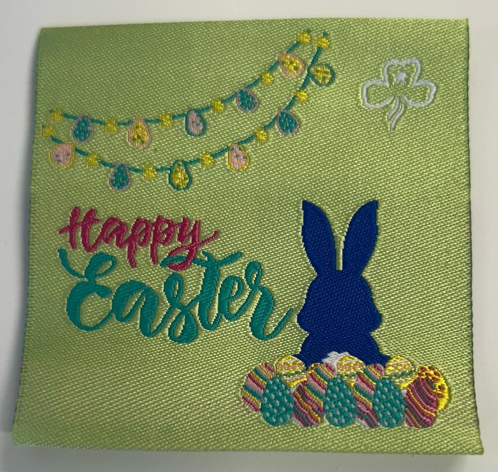 a light green square unbound badge with a blue bunny, easter eggs, the words happy easter and a garland of easter eggs