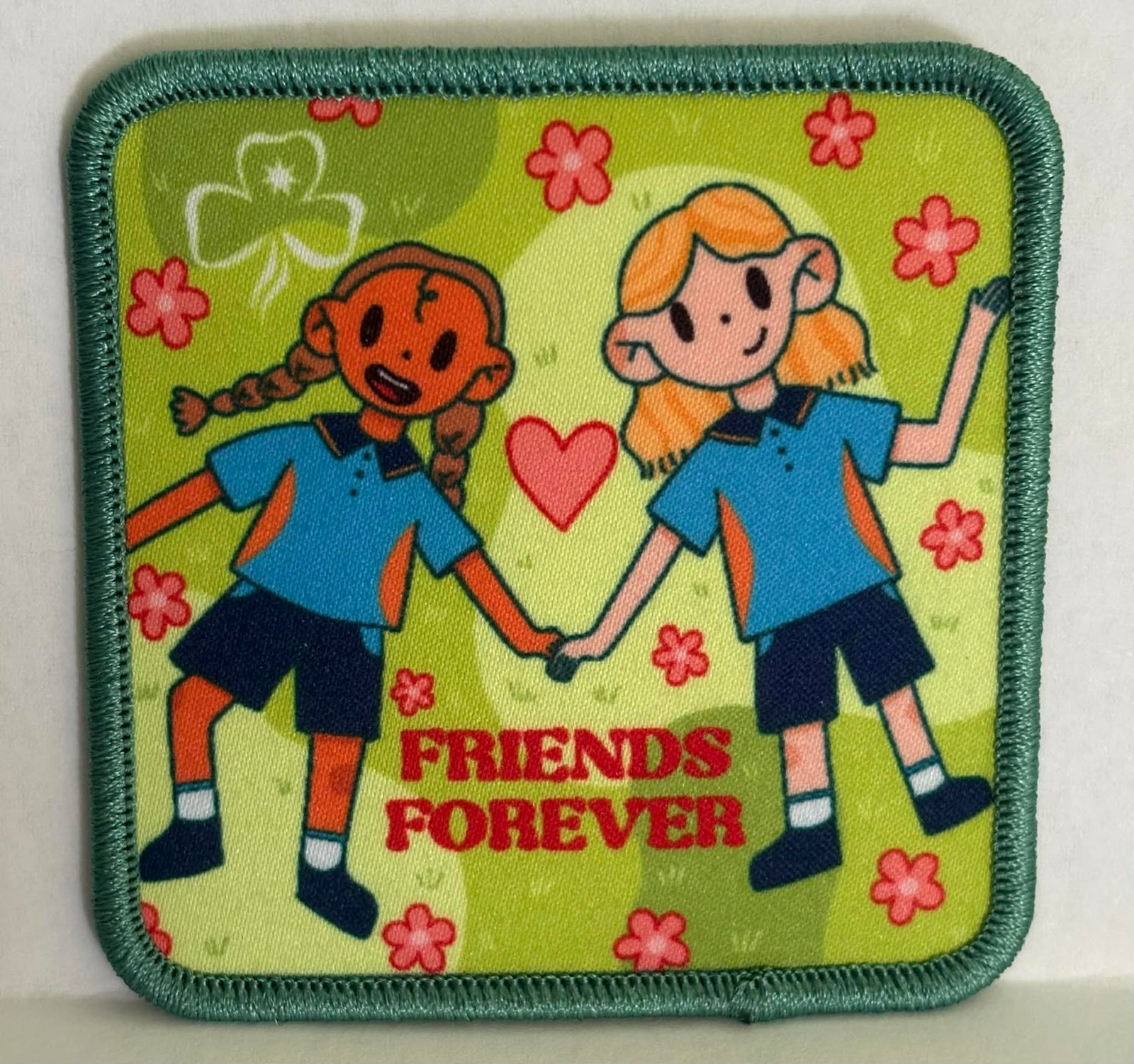 square badge with two girls holding hands and 'Friends Forever' text on a green background