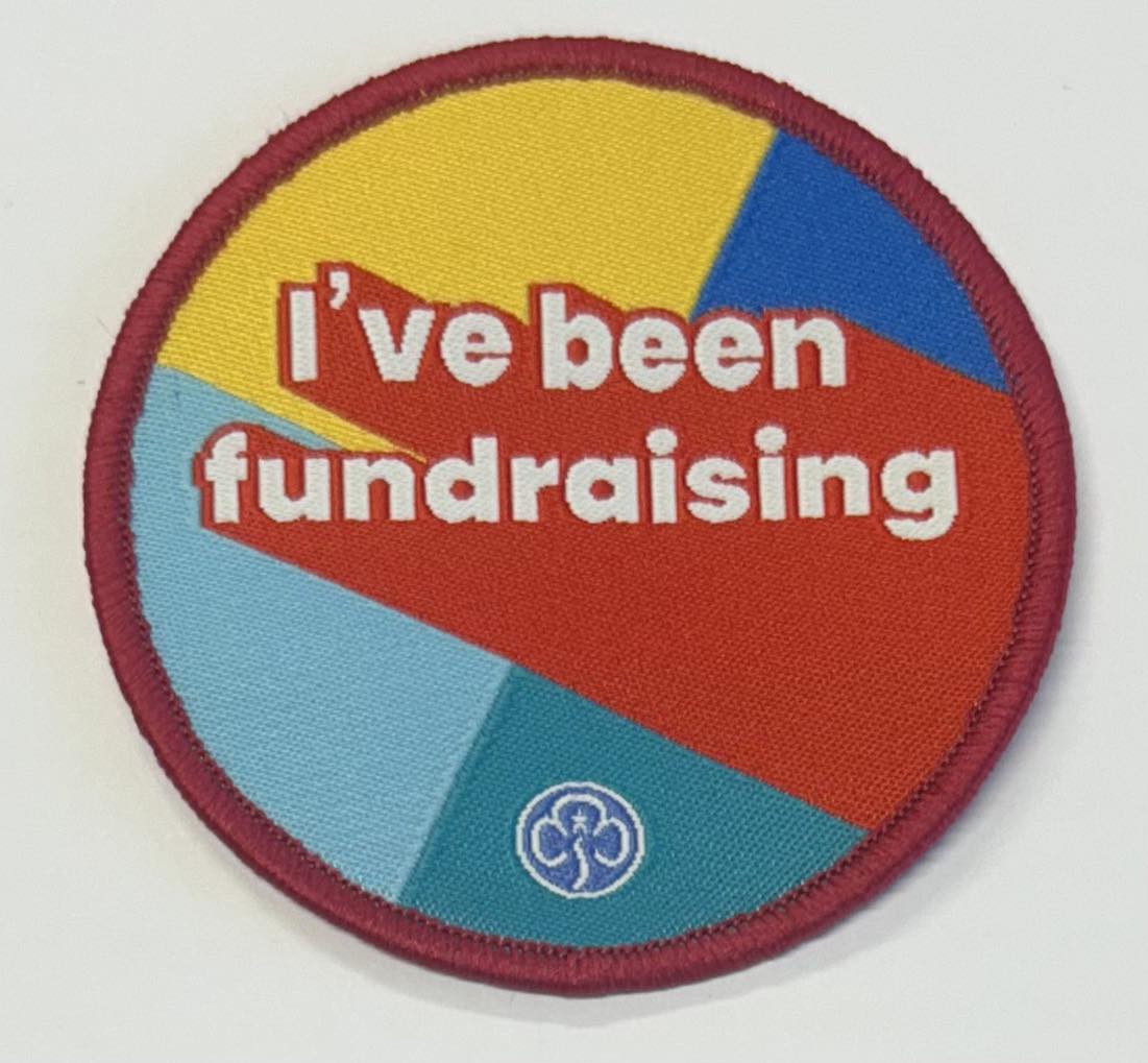 a round badge bound in red with yellow, royal blue, red, teal and light blue background with the words I've been fundraising