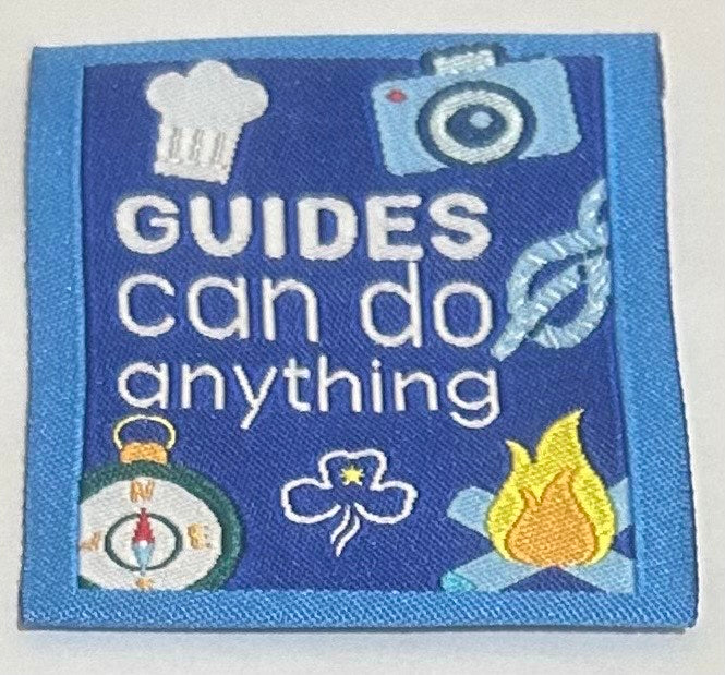 a square blue unbound  badge with guides can do anything written in white in the middle with a chefs hat, camera, compass and campfire
 