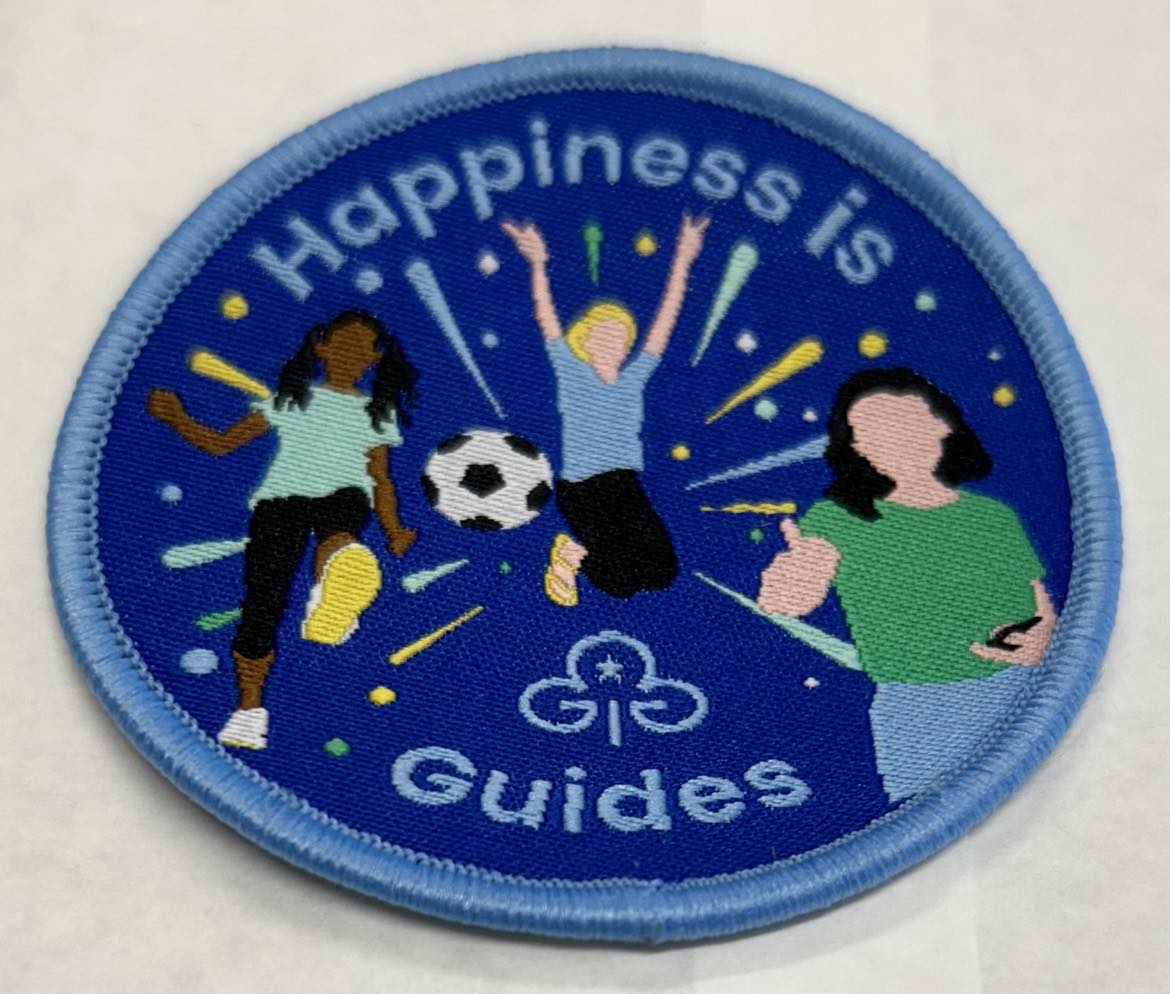 a round badge bound in blue with three girls and the words happiness is guides