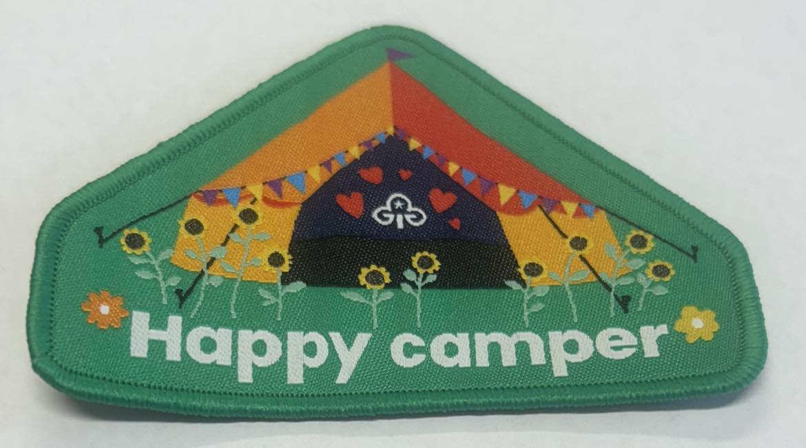 a triangle shaped badge bound in green with a tent and flowers on it