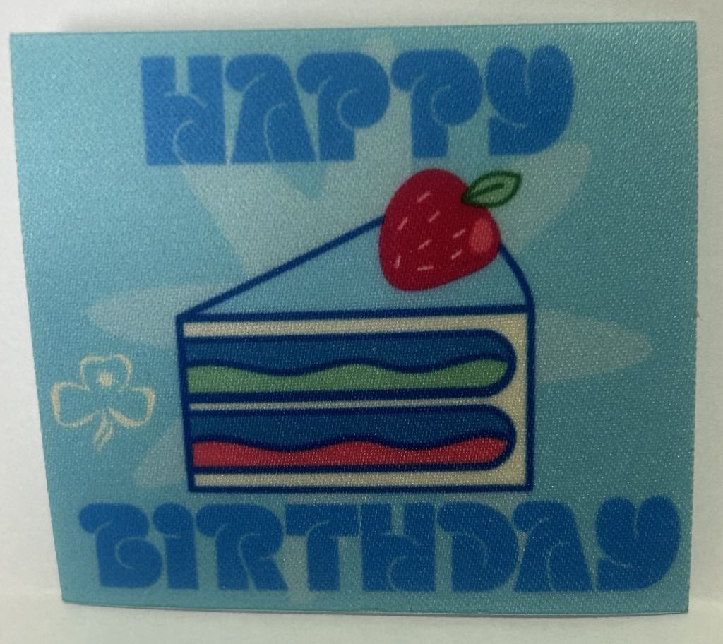 a square unbound badge with a slice of cake with a strawberry on top with the words happy birthday in blue