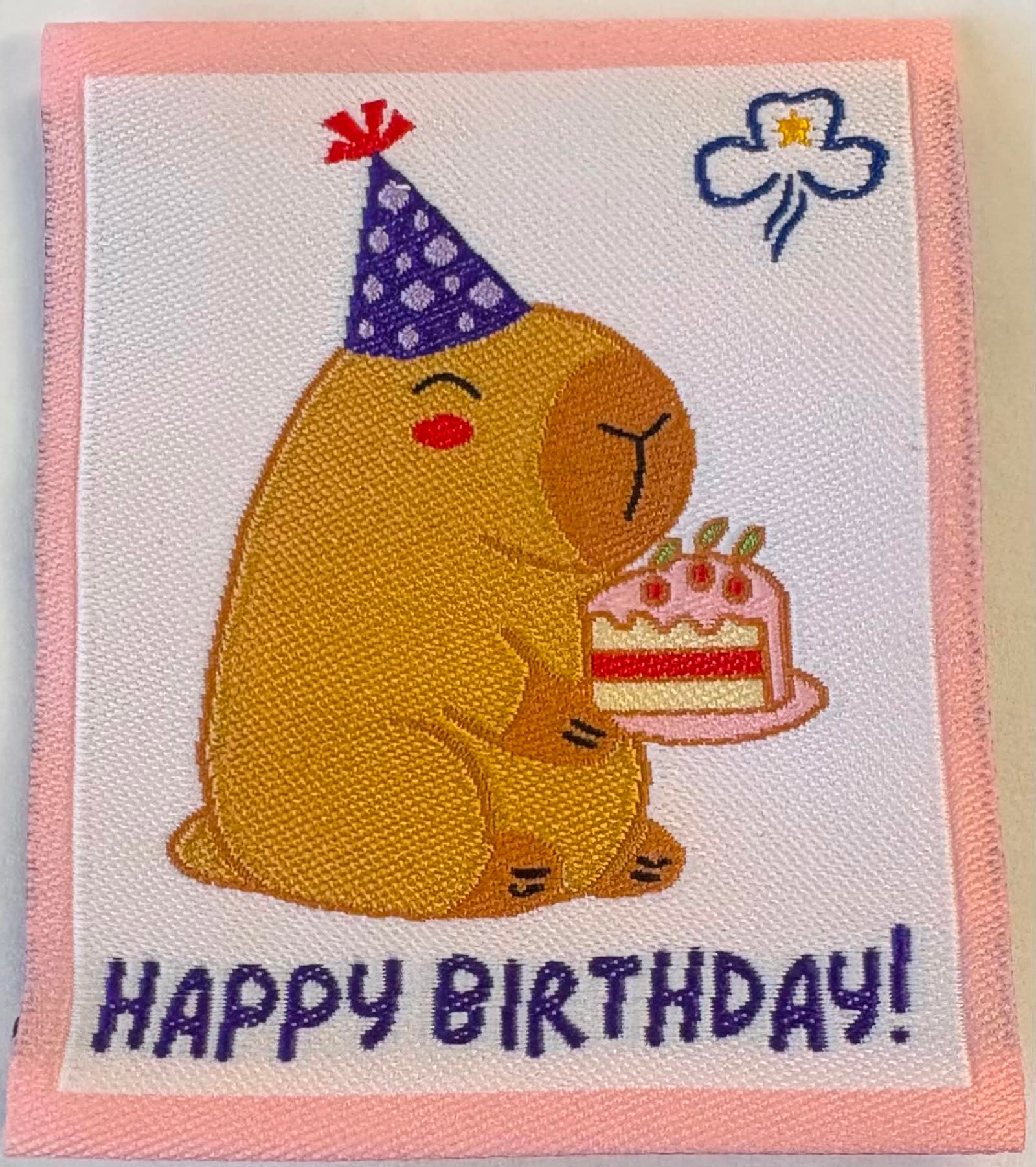 a square unbound badge with a Capybara with a party hat and holding a piece of cake