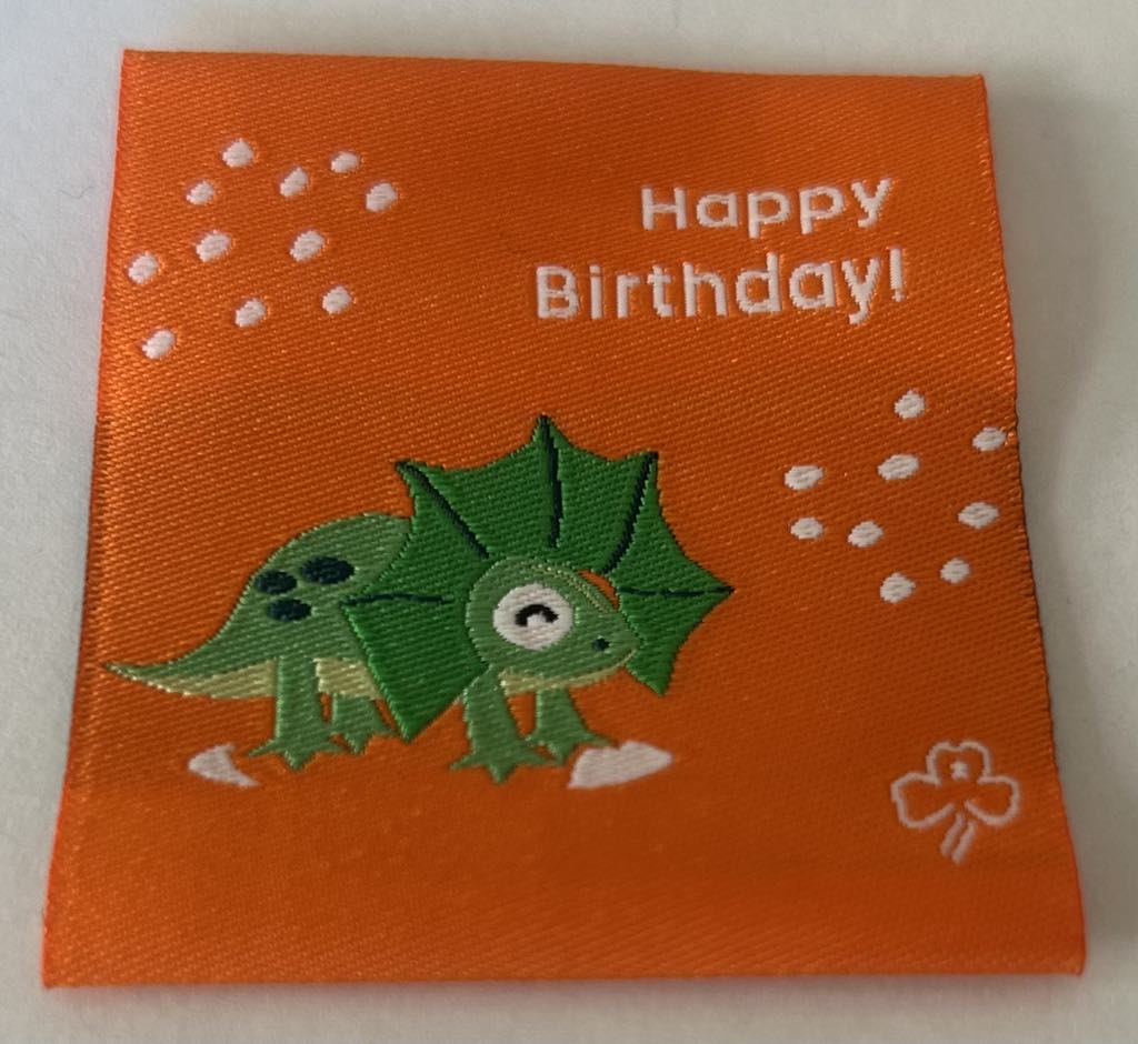 a square orange unbound badge with a green frill necked lizard with the words happy birthday
