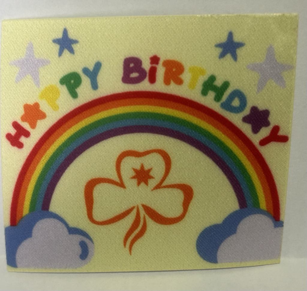 a square unbound badge with a yellow background with a rainbow and clouds and the words happy birthday written in multi colour letters
