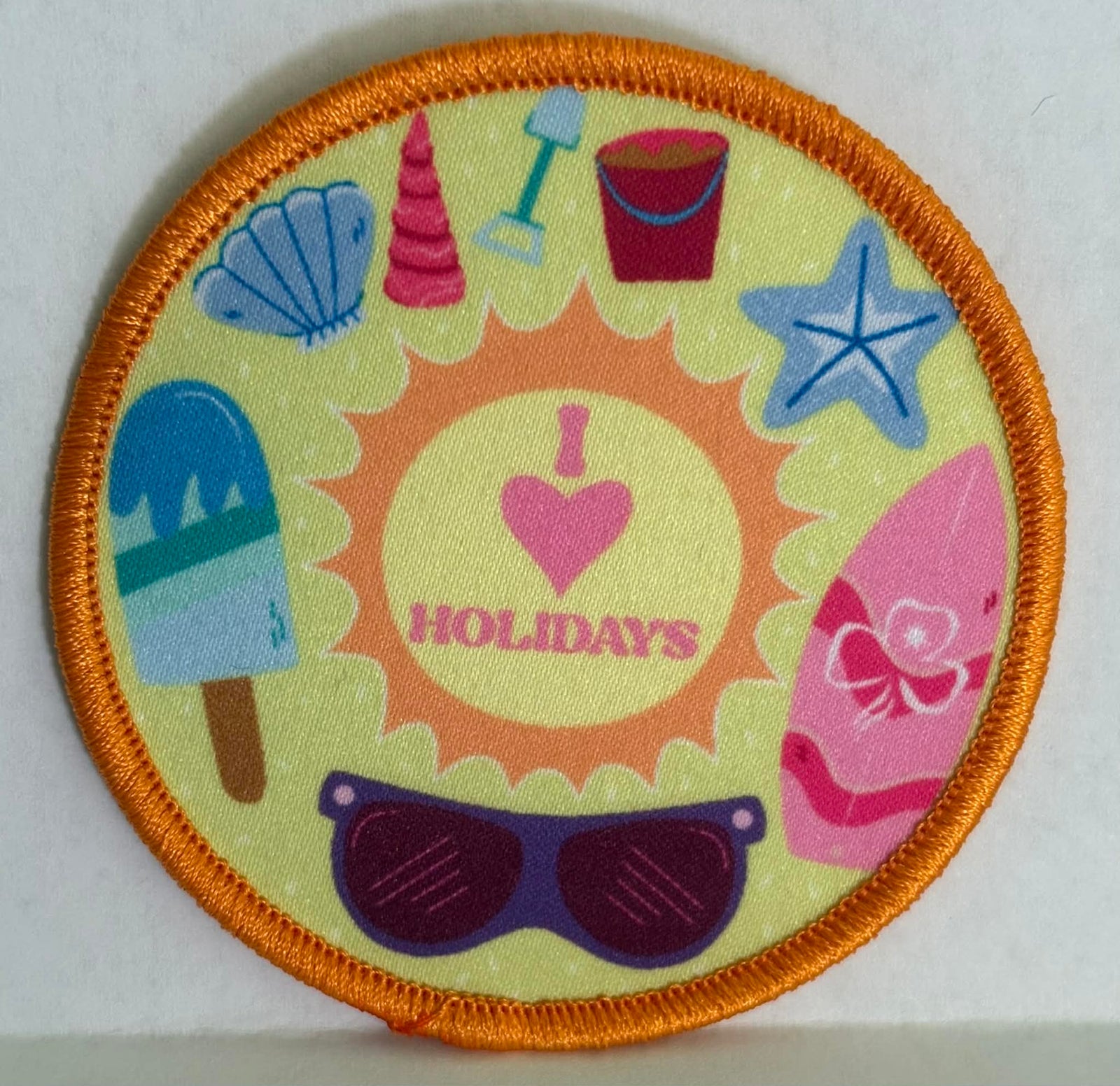 round yellow bound badge with gold trim  with beach-themed design featuring a sun, sunglasses, and summer items.