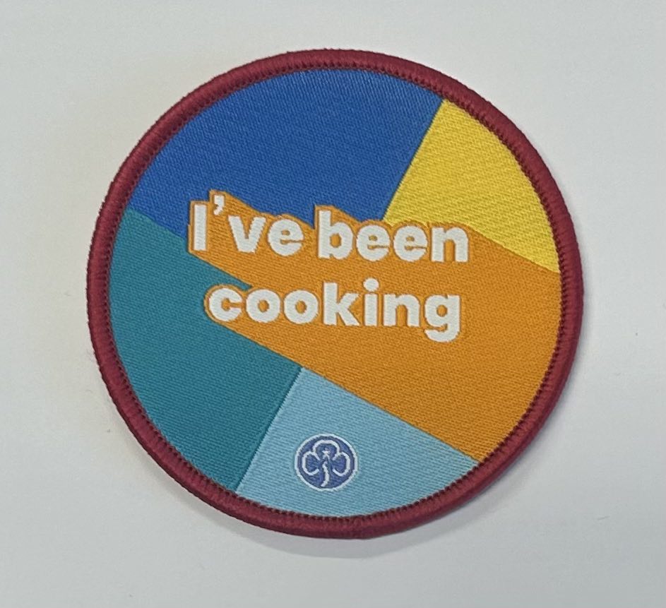 a round badge bound in red with royal blue, teal, light blue, orange and yellow background with the words I've been cooking