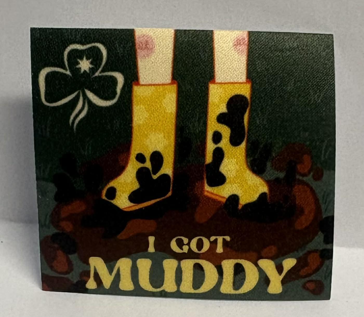 Square unbound badge with yellow gumboots and mud prints on a black background, featuring the text 'I Got Muddy'.