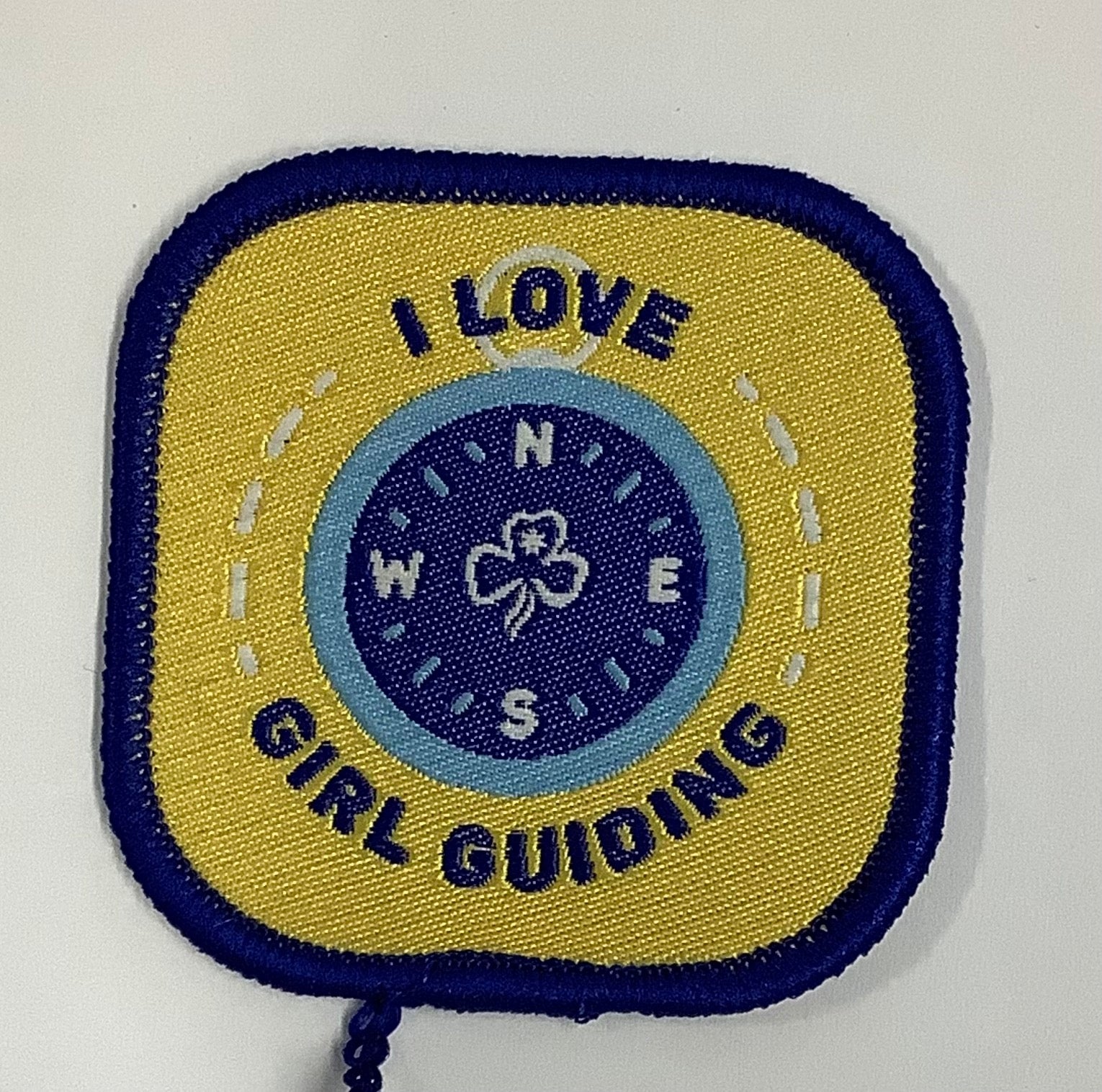 a square badge bound in blue with a compass in the middle of a yellow background