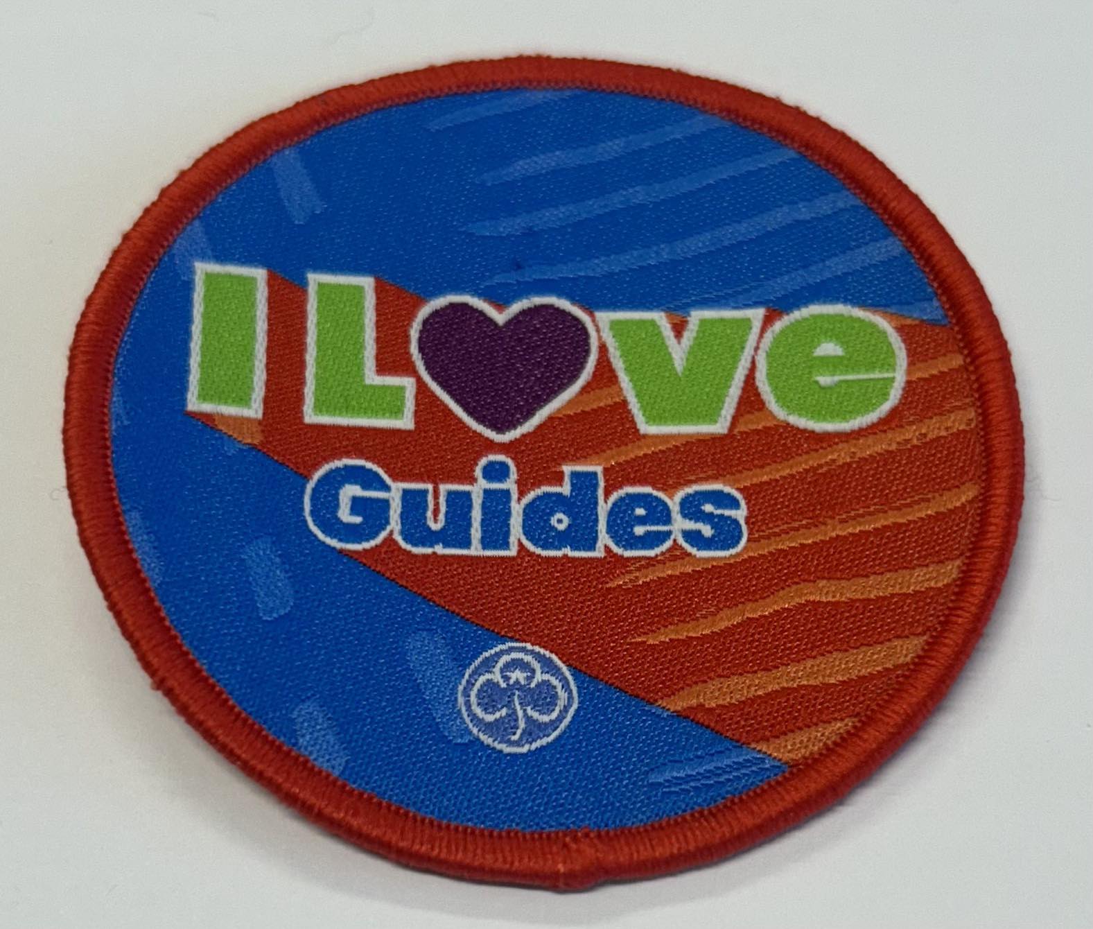 a round badge bound in red with a red and blue background with the words I love guides